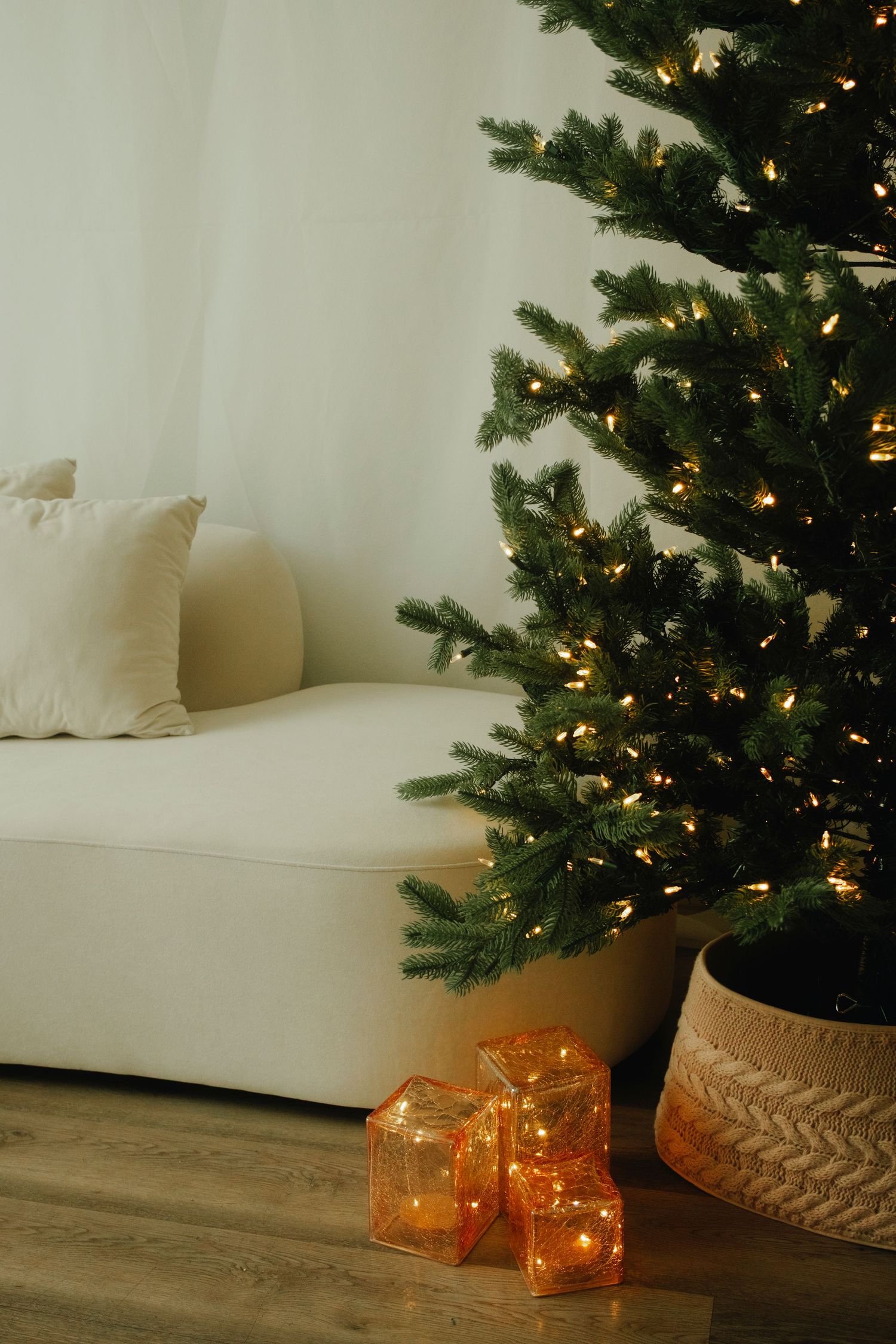 Cozy corner with illuminated Christmas tree and orange lanterns against white walls.
