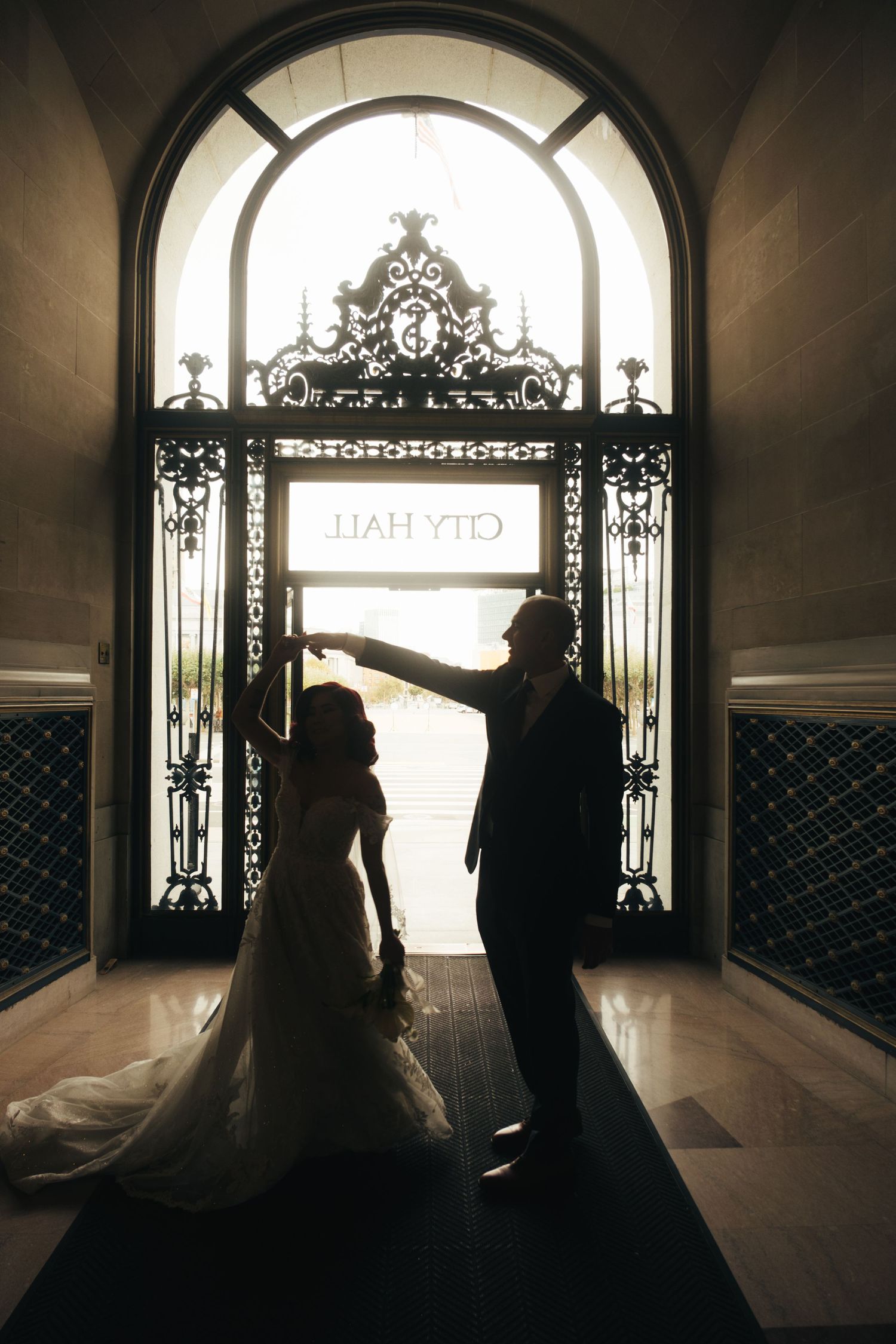 Dramatic silhouette of couple in wedding attire framed by grand archway and decorative ironwork.