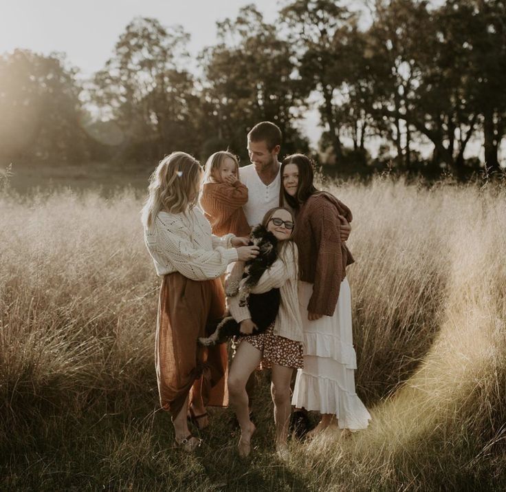 Family gathered together in tall grass field during sunset photoshoot.