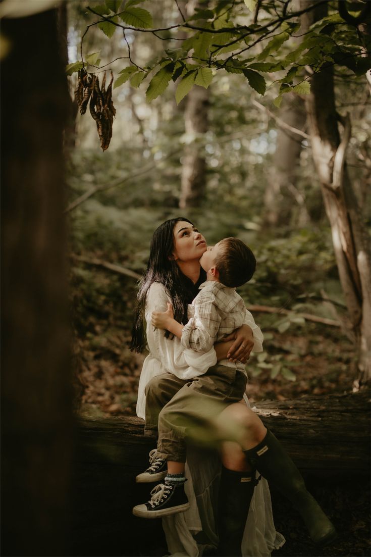 Romantic forest photoshoot with couple sitting on fallen log in dappled sunlight.