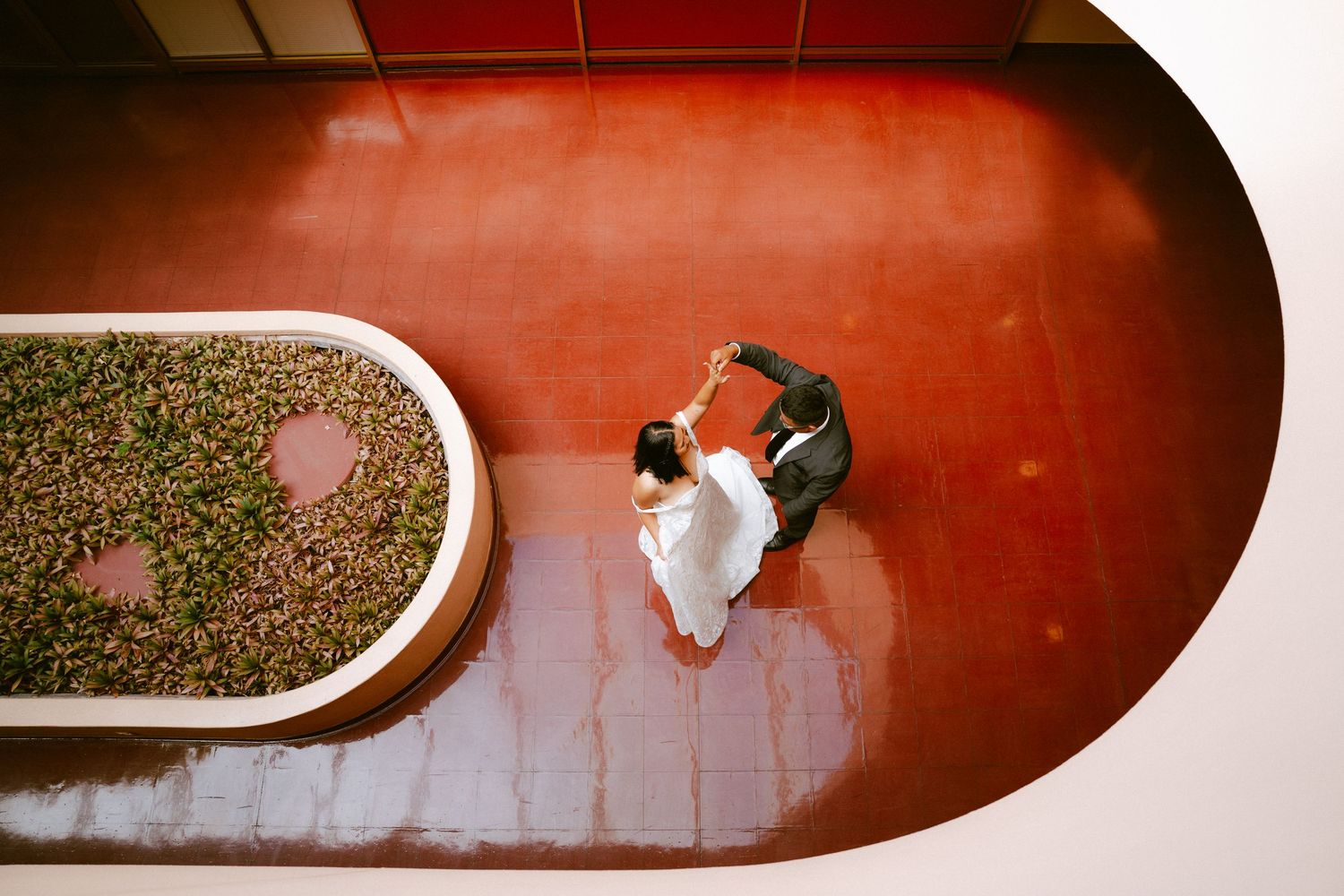 Aerial view of a couple dancing on a red floor beside a lush green garden bed in an elegant venue.