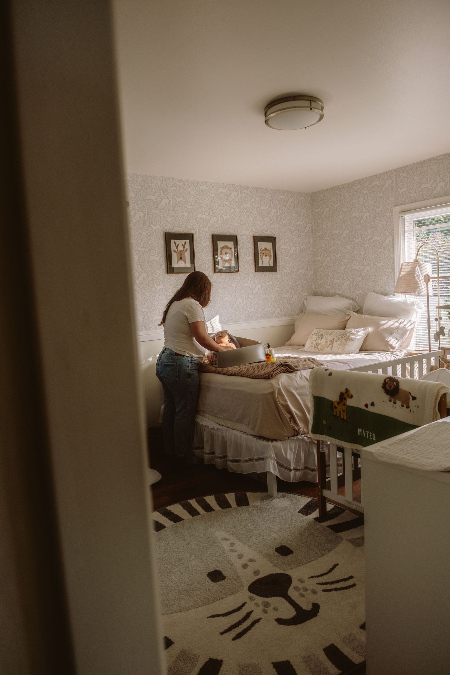 Woman arranging items in a cozy nursery with animal-themed decor, white crib, and patterned rug.