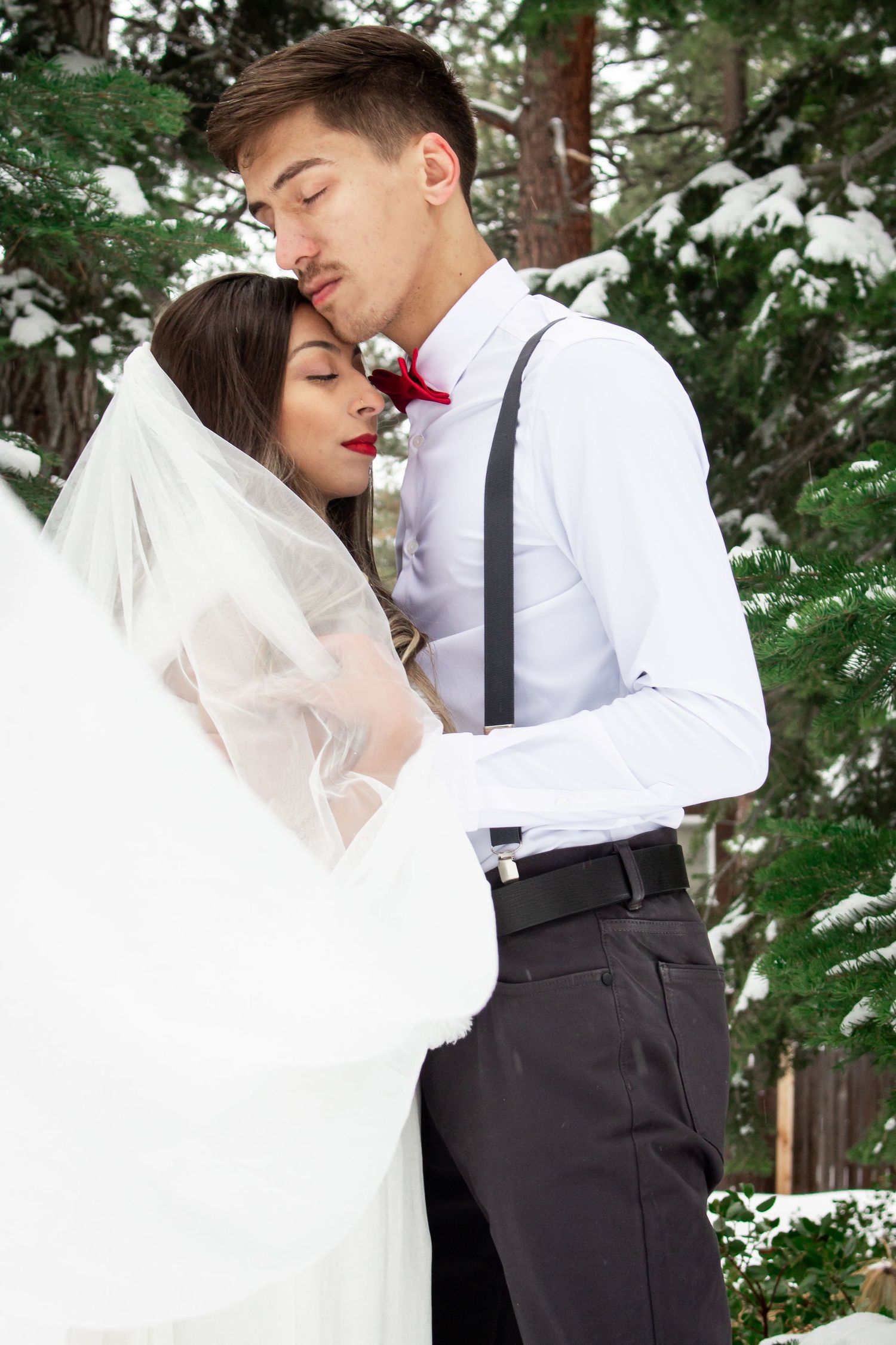 Intimate winter wedding portrait with snow-covered pine trees in background.