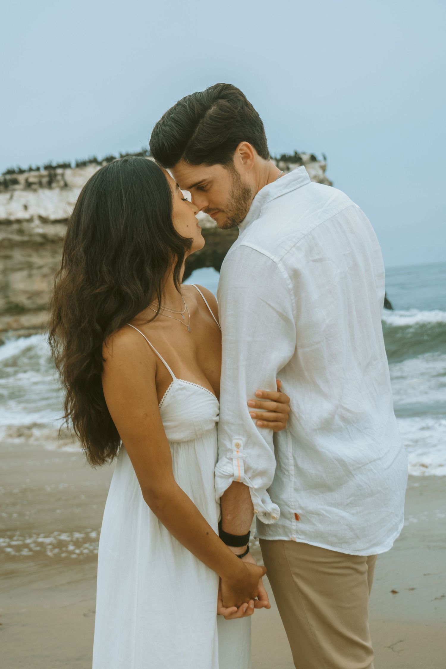 Romantic couple in white embracing on a sandy beach during an intimate photoshoot.