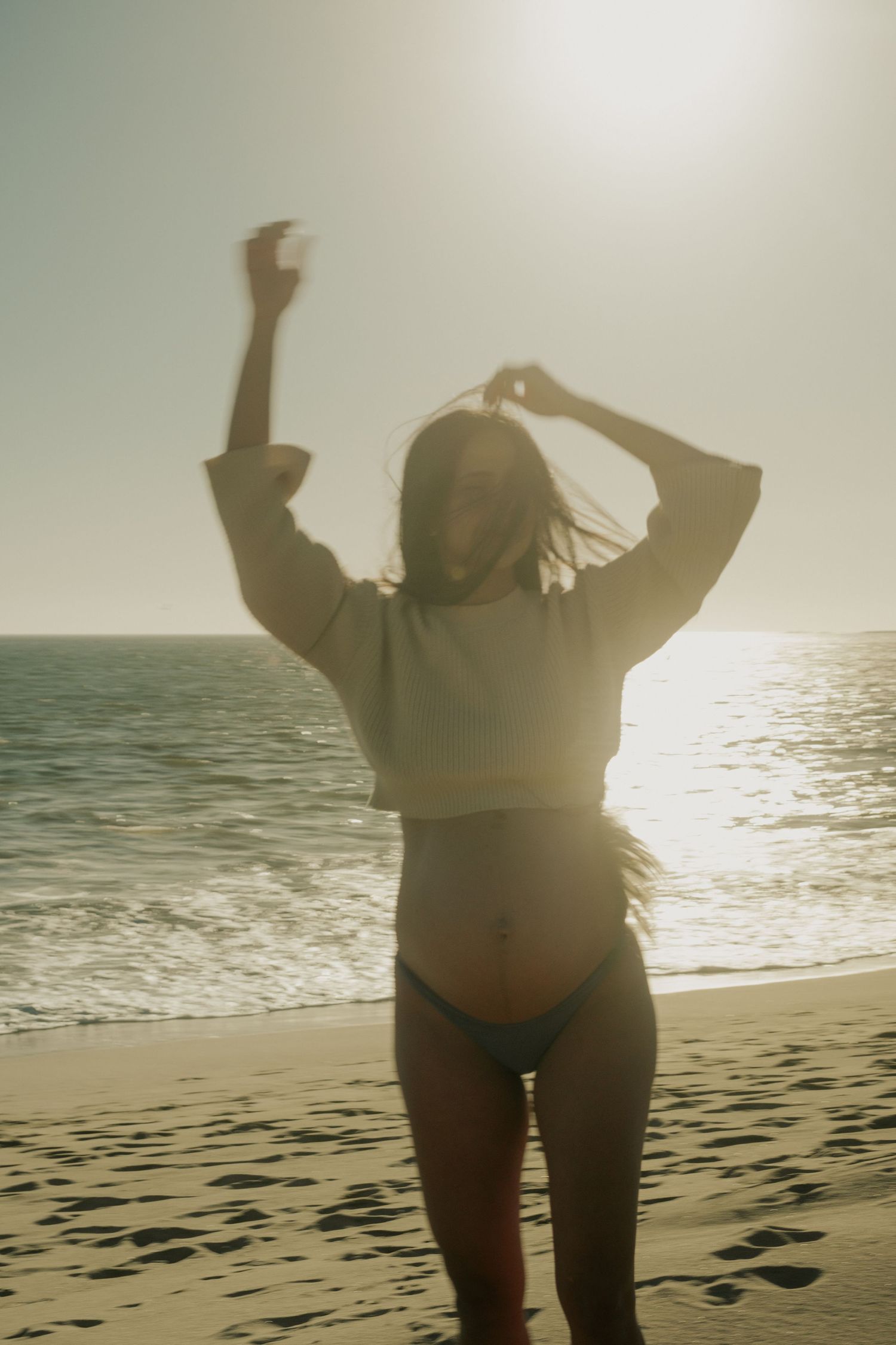 Silhouetted figure with arms raised celebrating on beach at sunset.