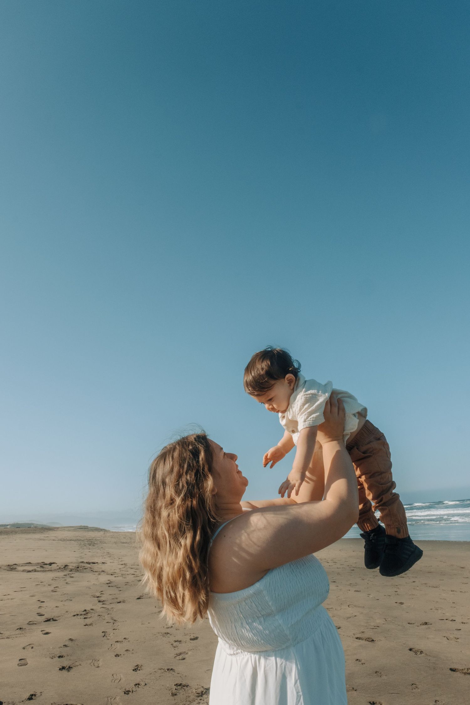 A series of playful moments on a beach showing a person in white lifting a small child against a blue sky backdrop.