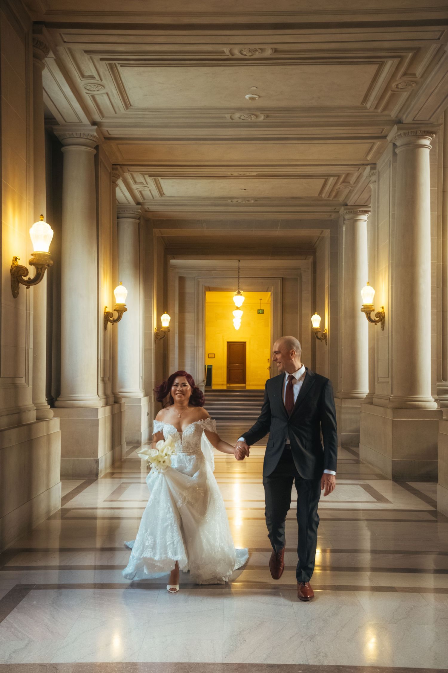 Wedding couple dancing and twirling in a luxurious marble hallway with classical architecture.