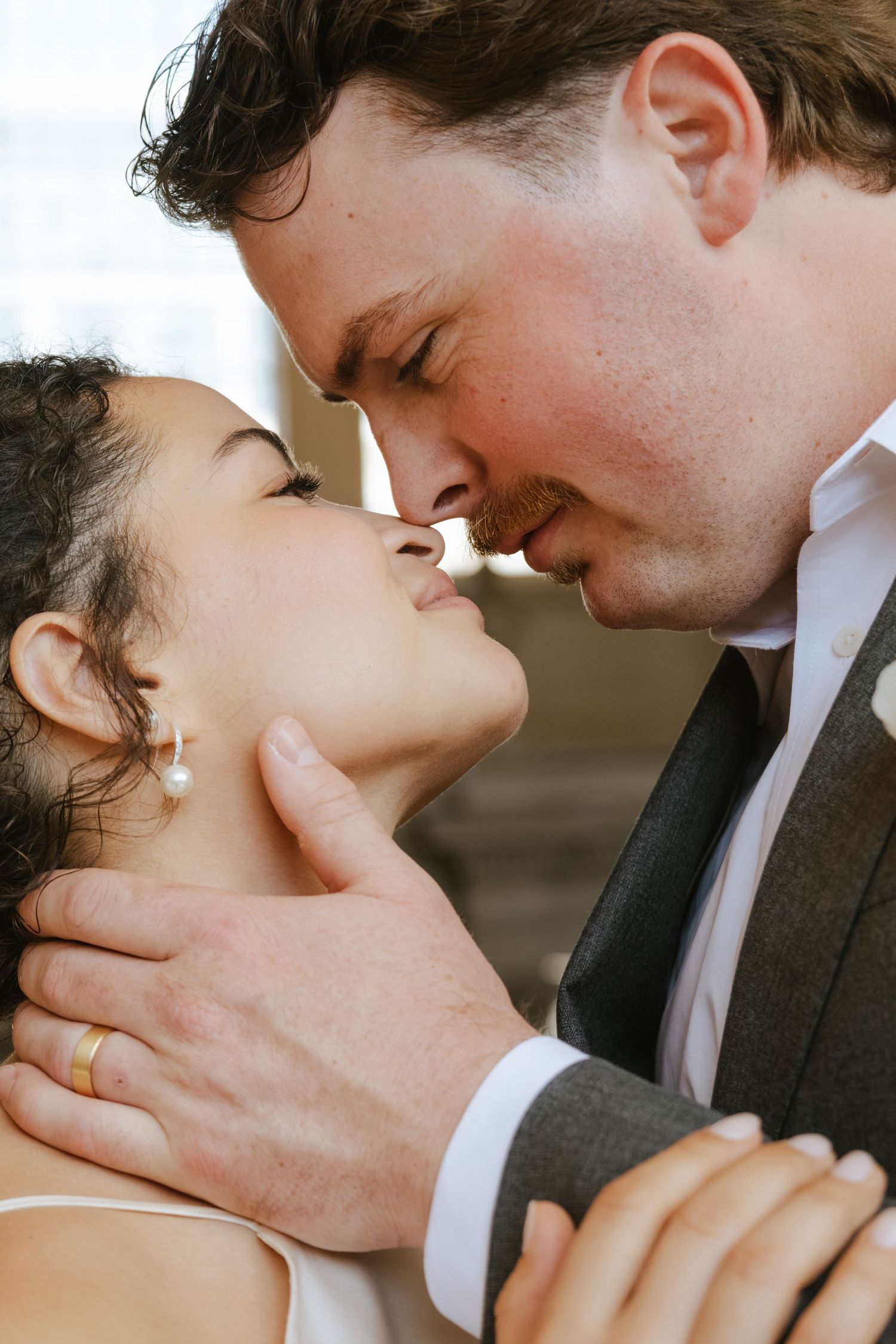 A couple shares an intimate moment, nearly kissing, as the groom tenderly holds the bride's face on their wedding day.