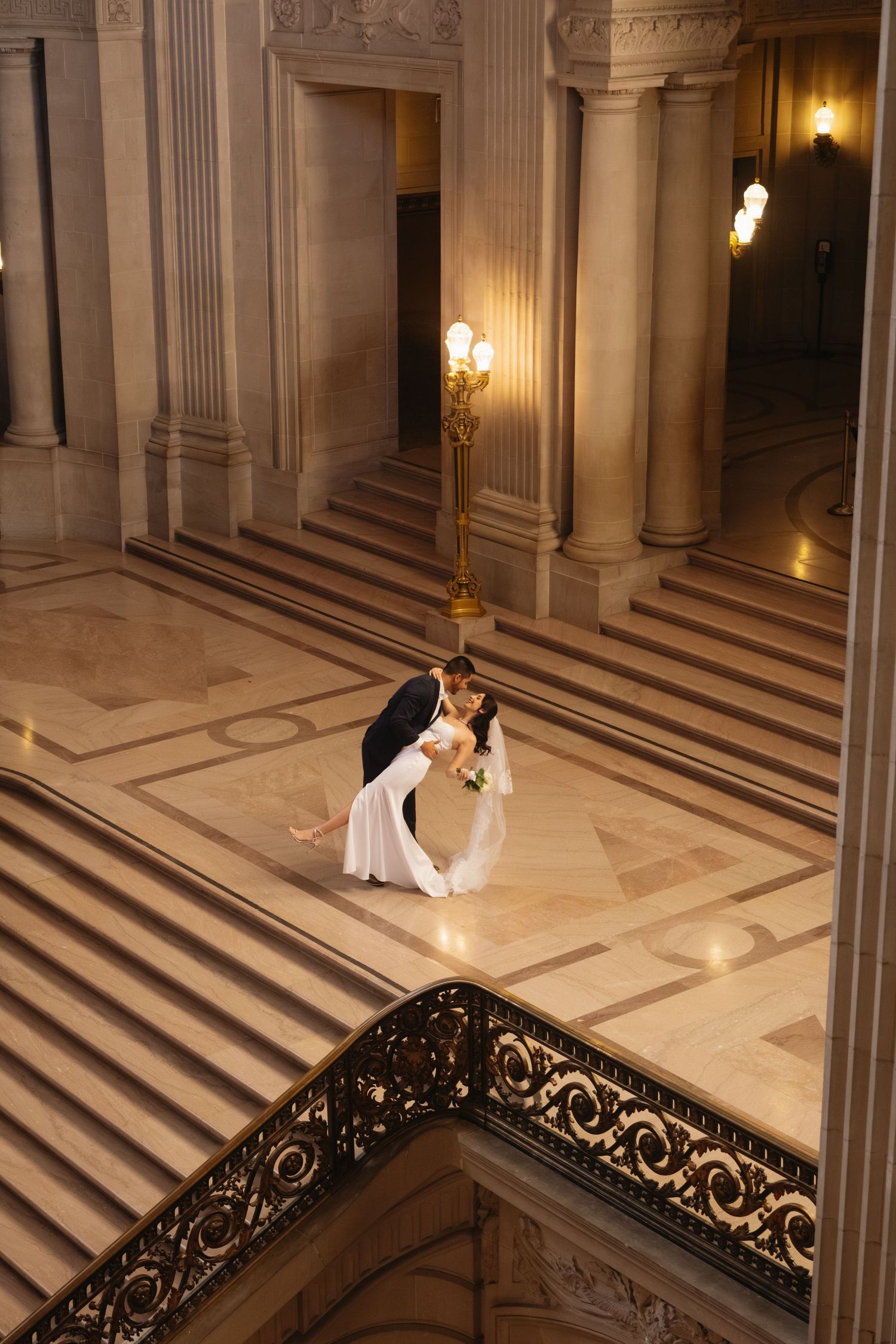 A couple shares a romantic dance in an elegant marble hall with ornate columns and glowing wall sconces.