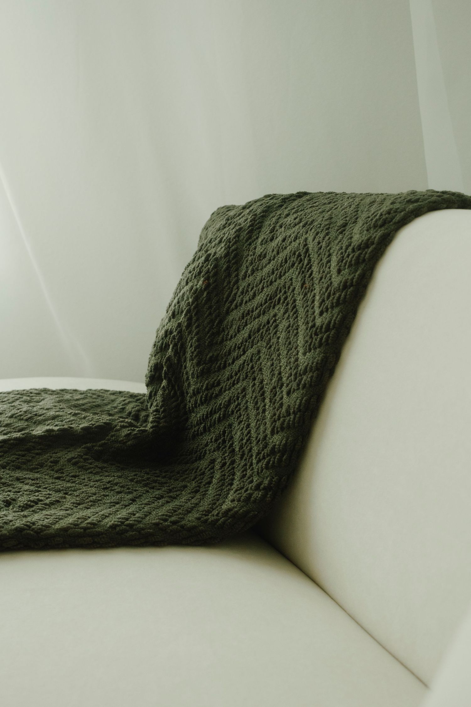 Gray knit throw blanket artfully draped over white modern sofa corner.