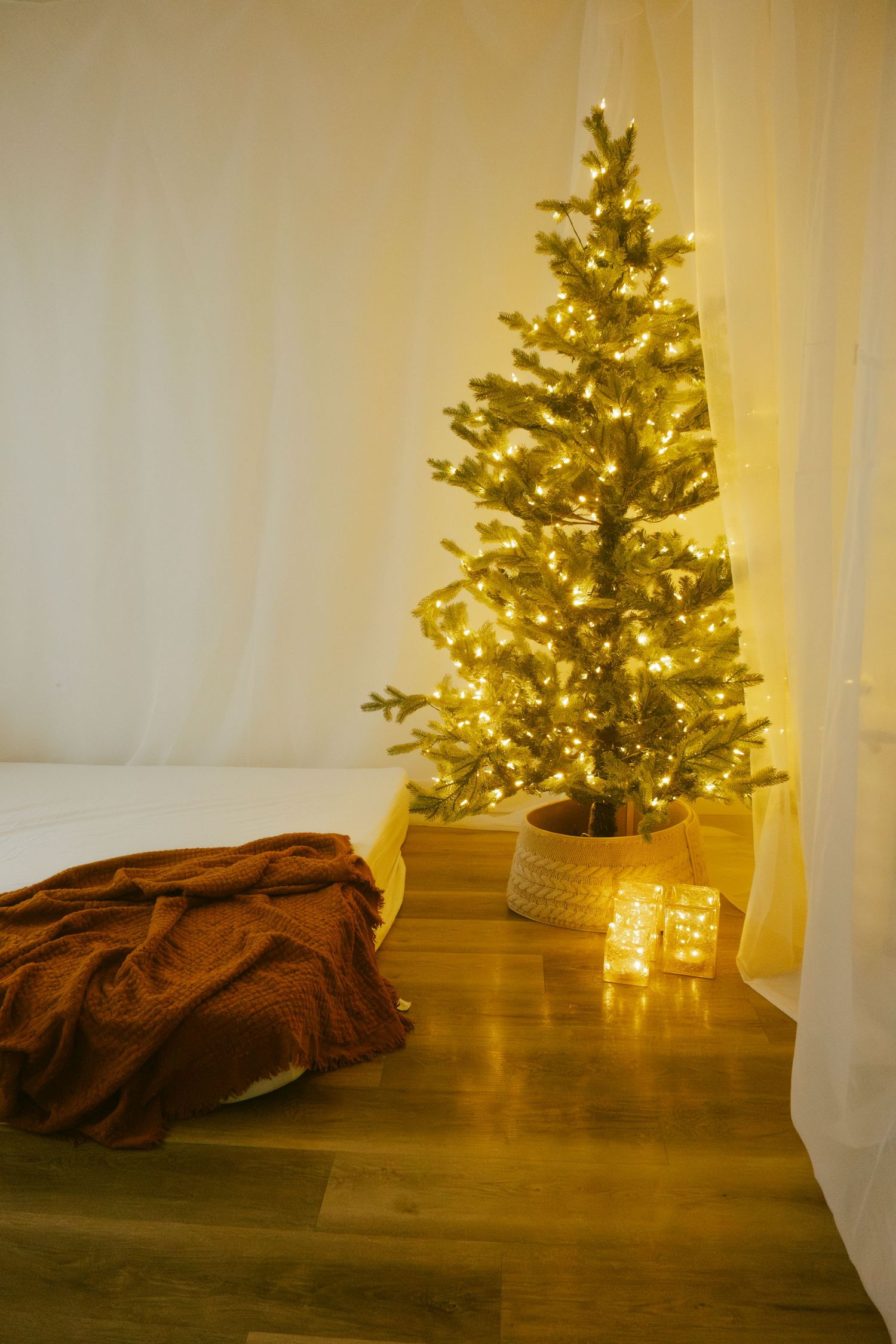 Christmas tree with golden lights casting warm glow on wooden floor with brown textile.