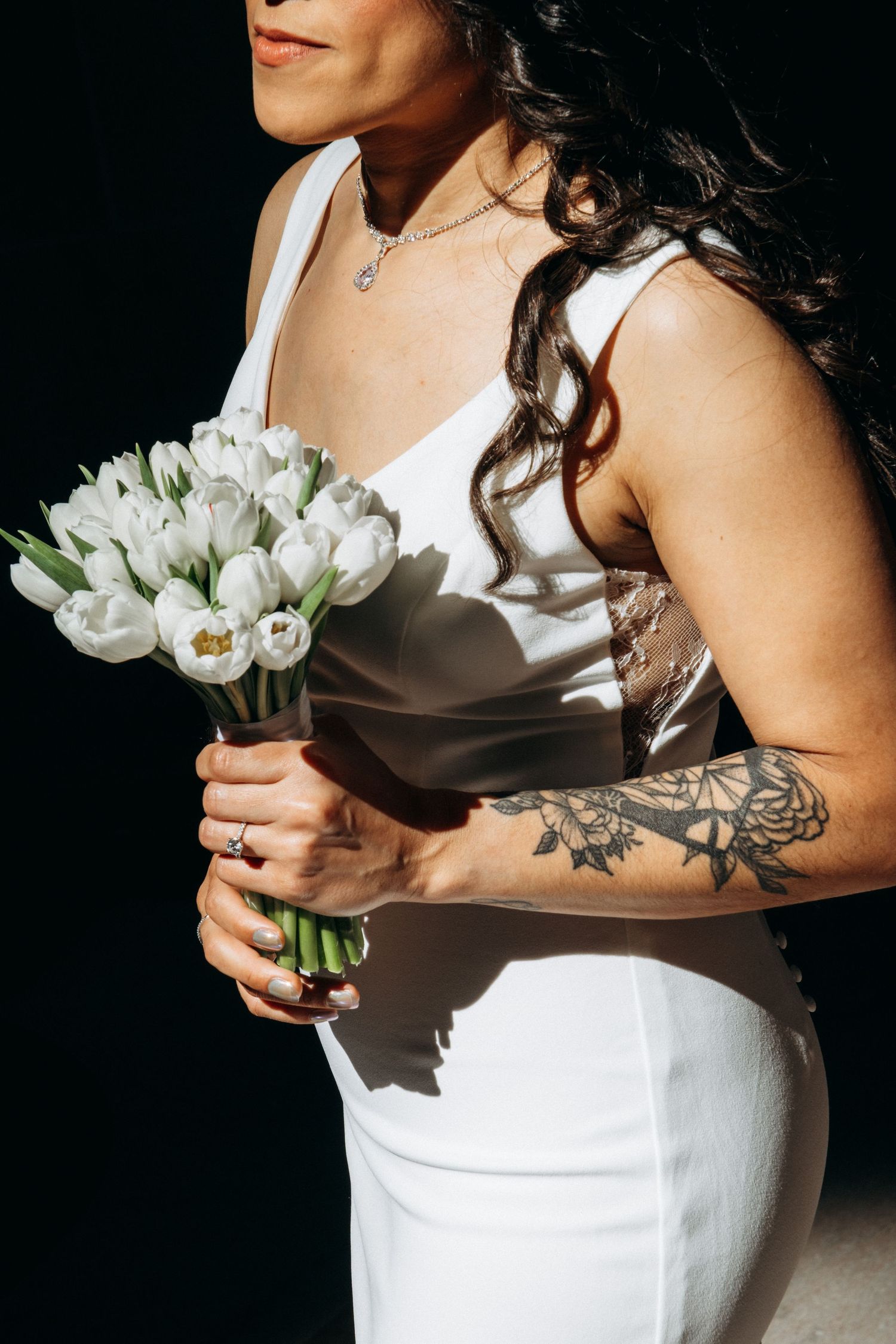 A person in a white dress holds a bouquet of white tulips against a dark background.