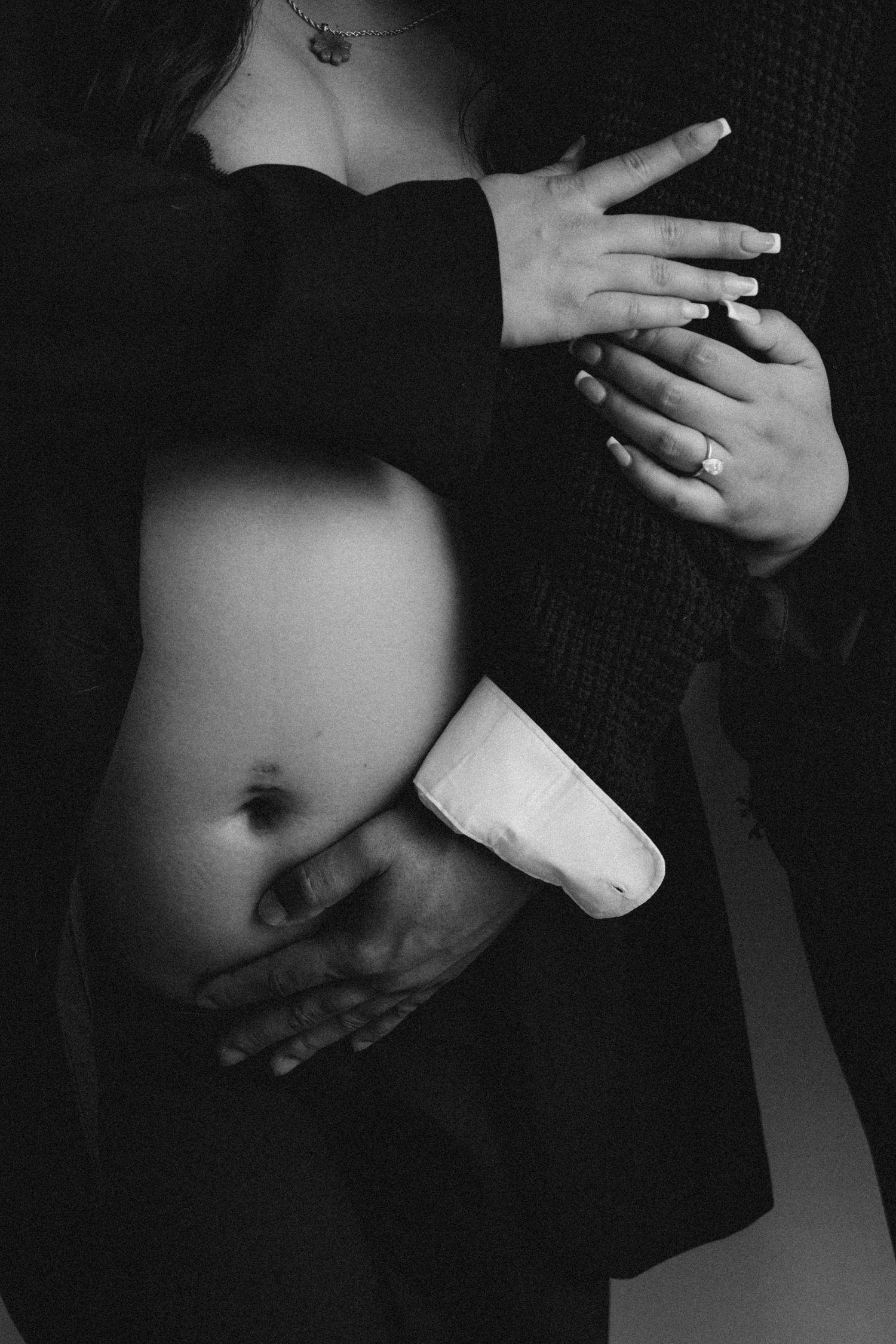 A black and white artistic photo showing hands resting on a pregnant belly.