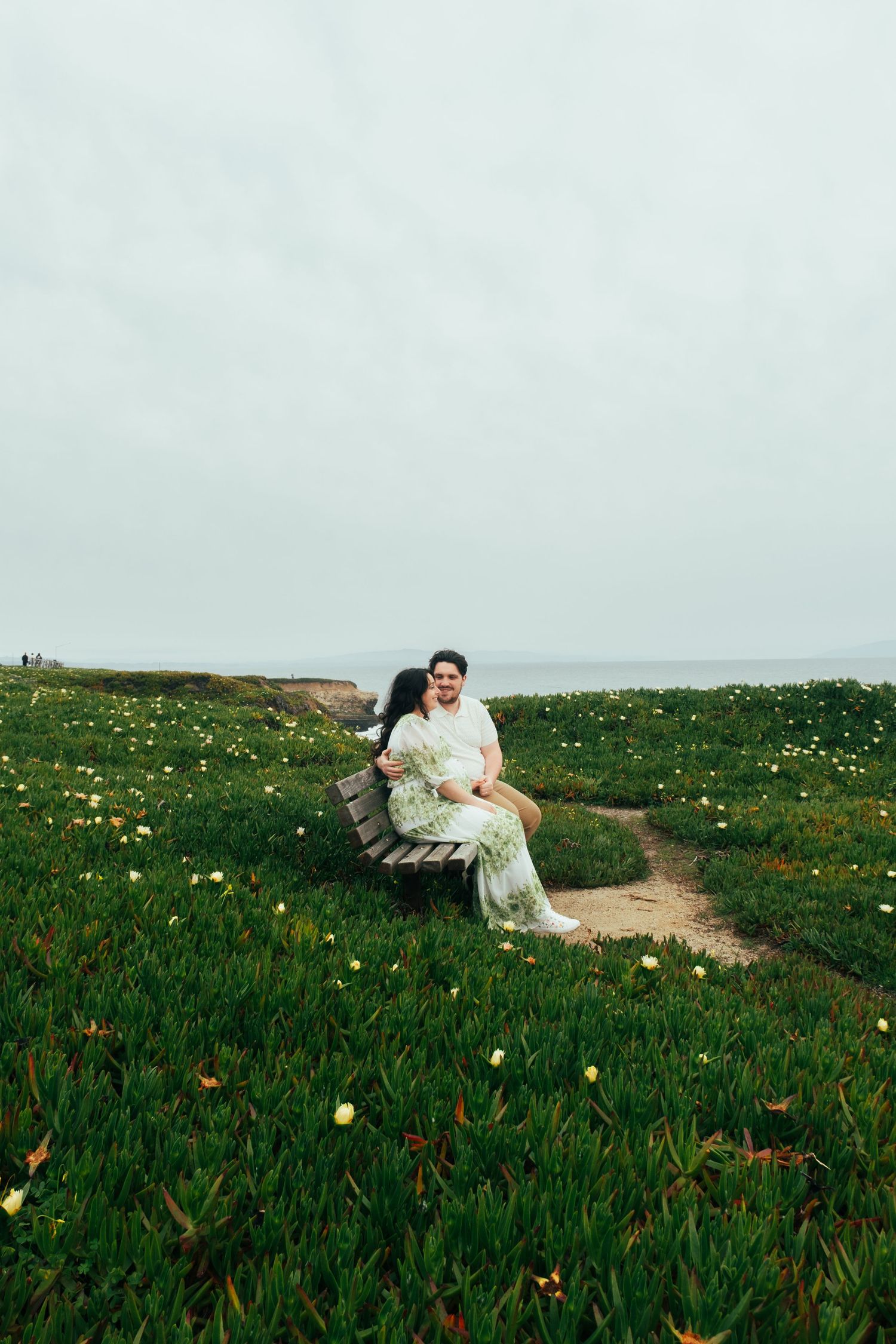Couple sitting in a field of yellow wildflowers with green grass on a cloudy day.