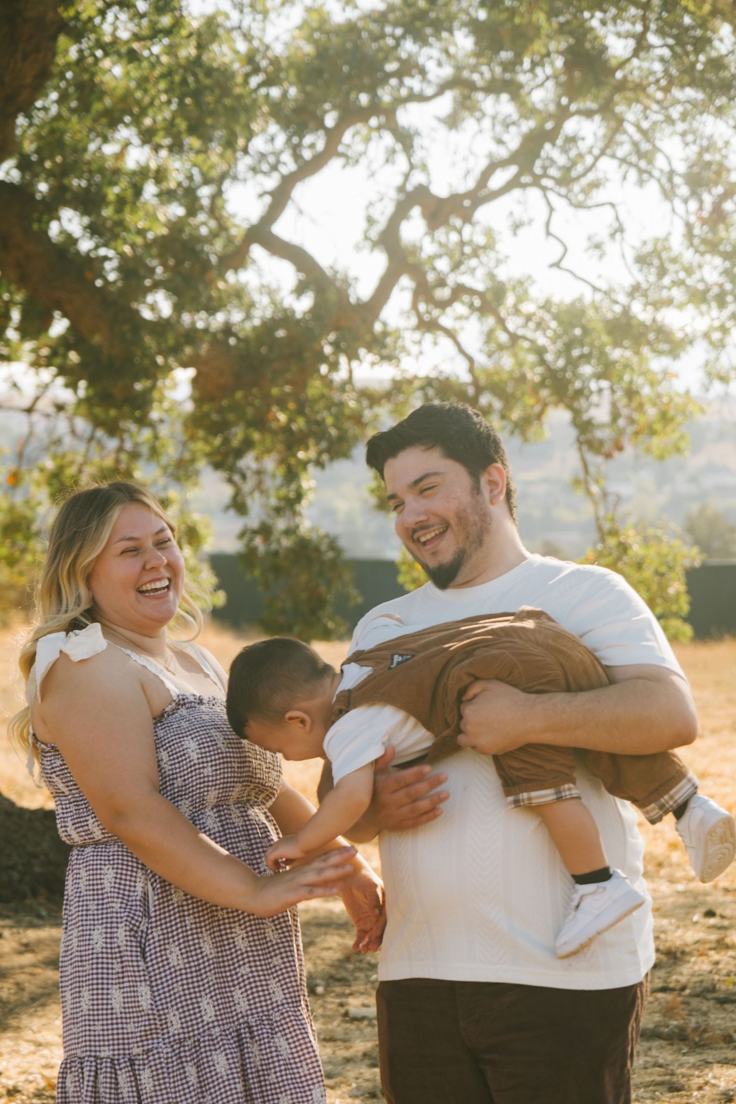 Candid family laughter during outdoor photo session in golden sunlight.