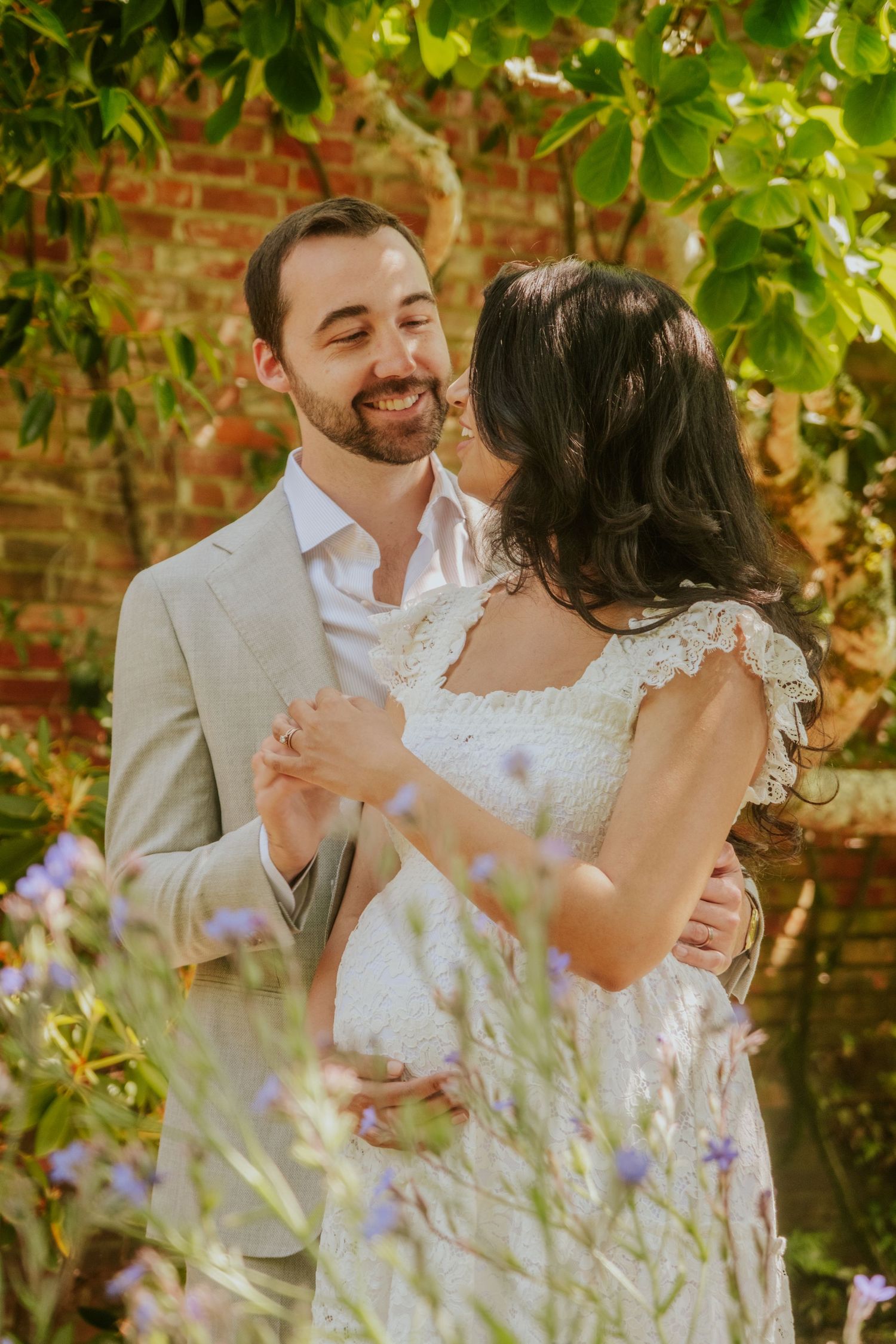 Romantic couple embracing in garden with flowering vines and brick wall.