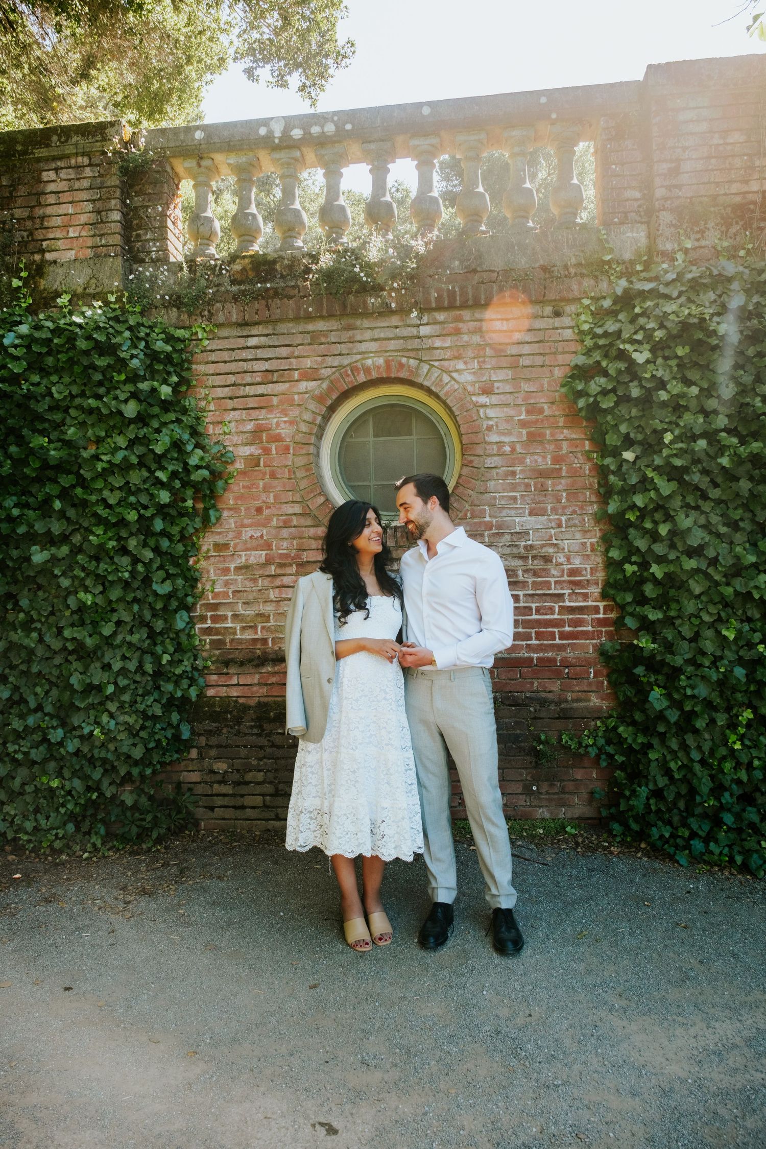 A romantic couple poses against a rustic brick wall covered in ivy during an engagement session.