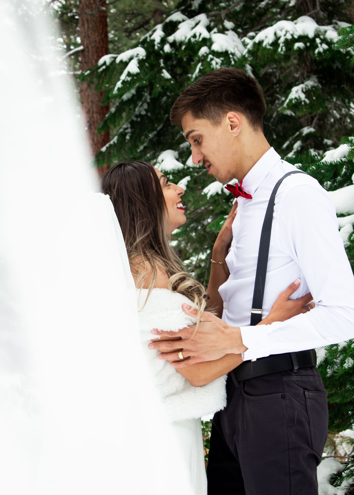 Romantic winter wedding moment captured among snow-covered evergreen trees.
