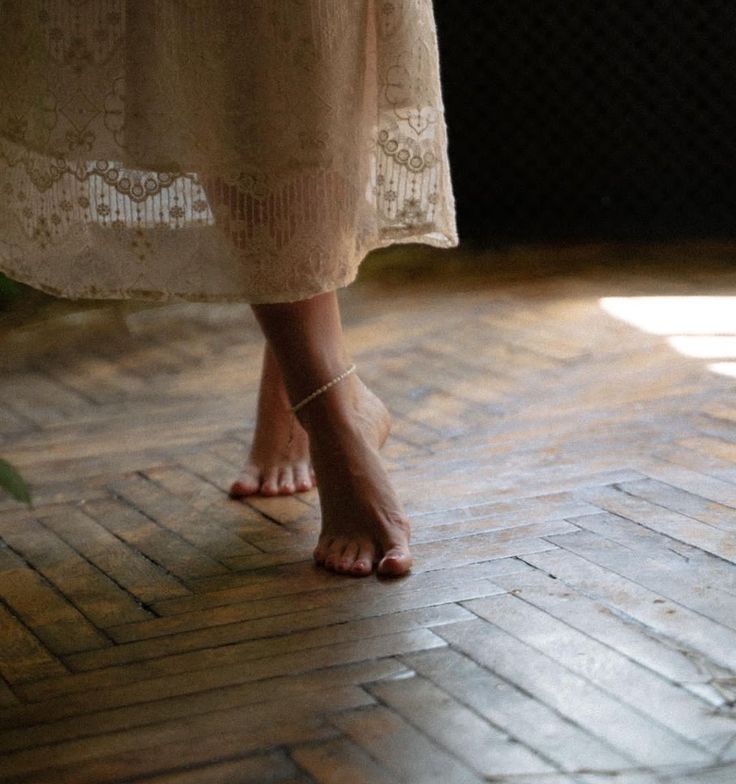 A sequence of bare feet walking across weathered wooden floorboards in soft natural lighting.
