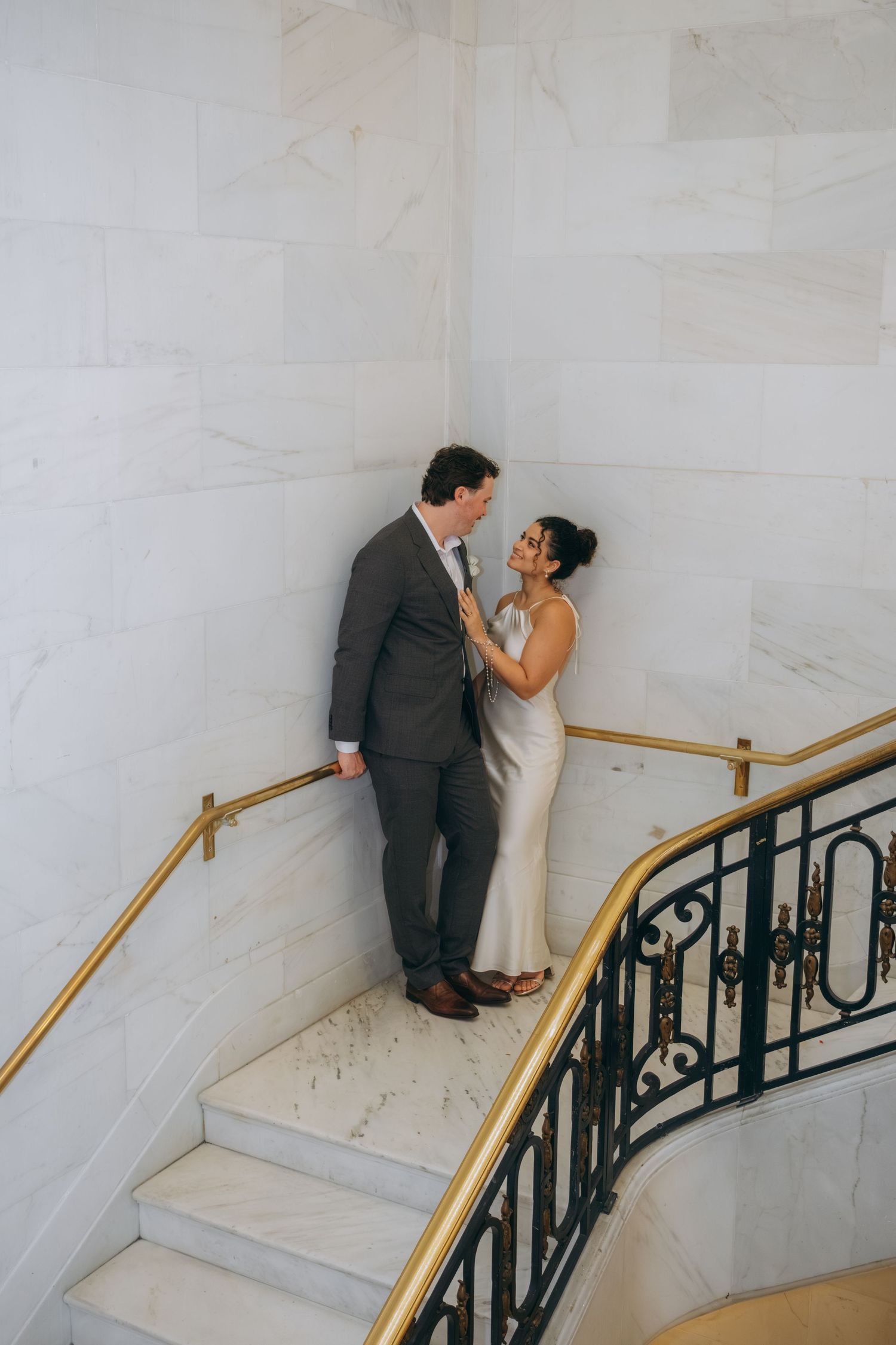 Bride and groom share a romantic moment on marble stairs with gold railings inside San Francisco City Hall.