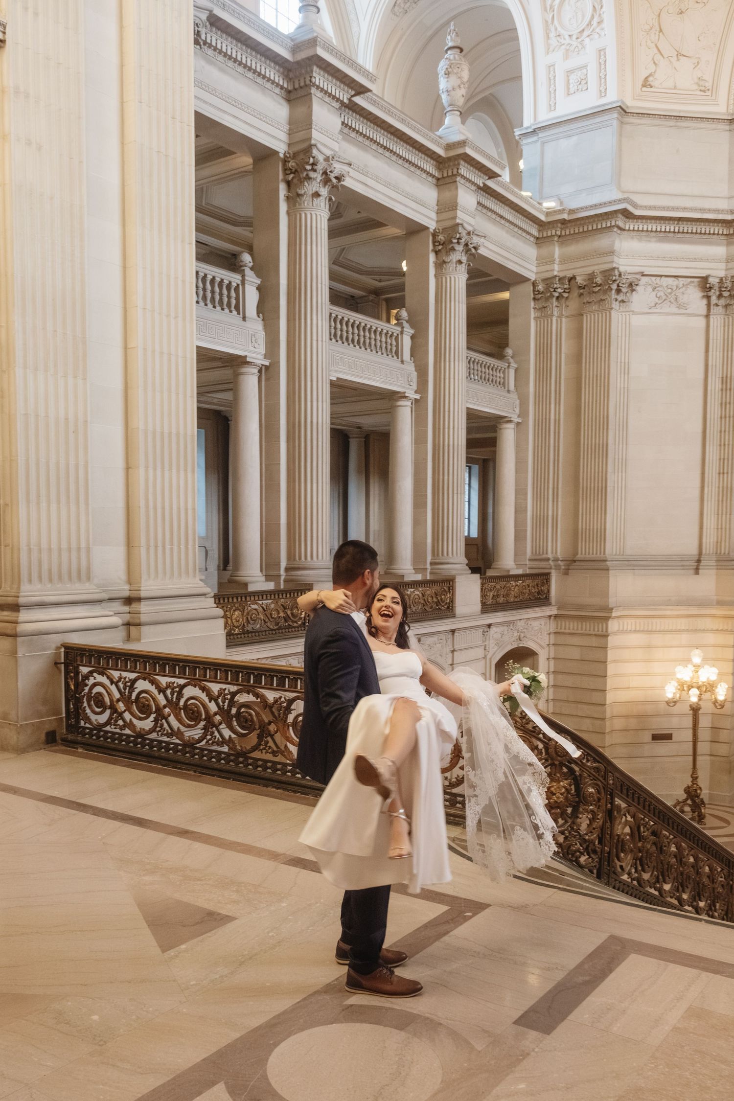 Wedding couple shares intimate dance poses in a grand marble hallway with classical architecture.