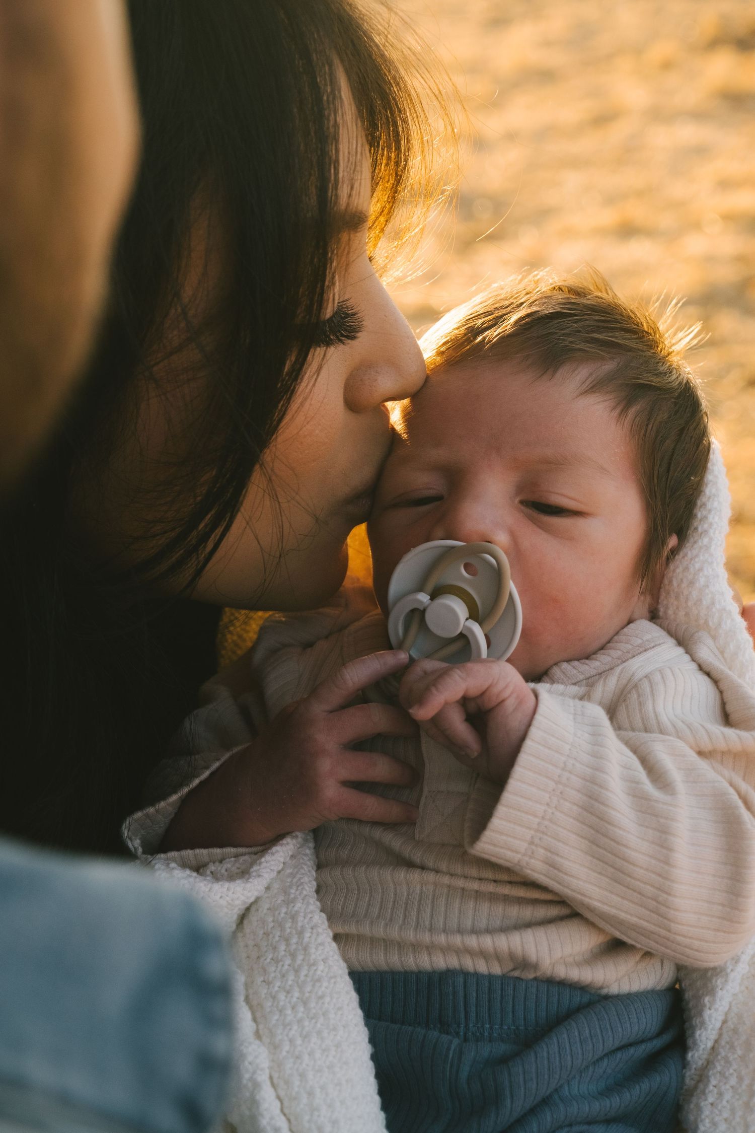 Tender moment between parent and sleeping baby in warm sunset lighting.