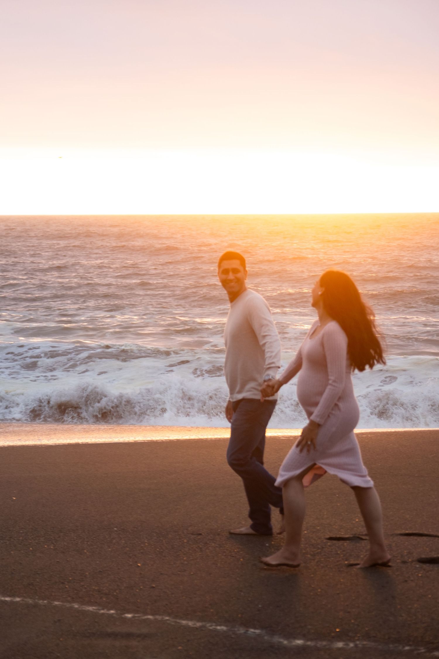 Couple playing and laughing together on a beach during golden sunset hours.