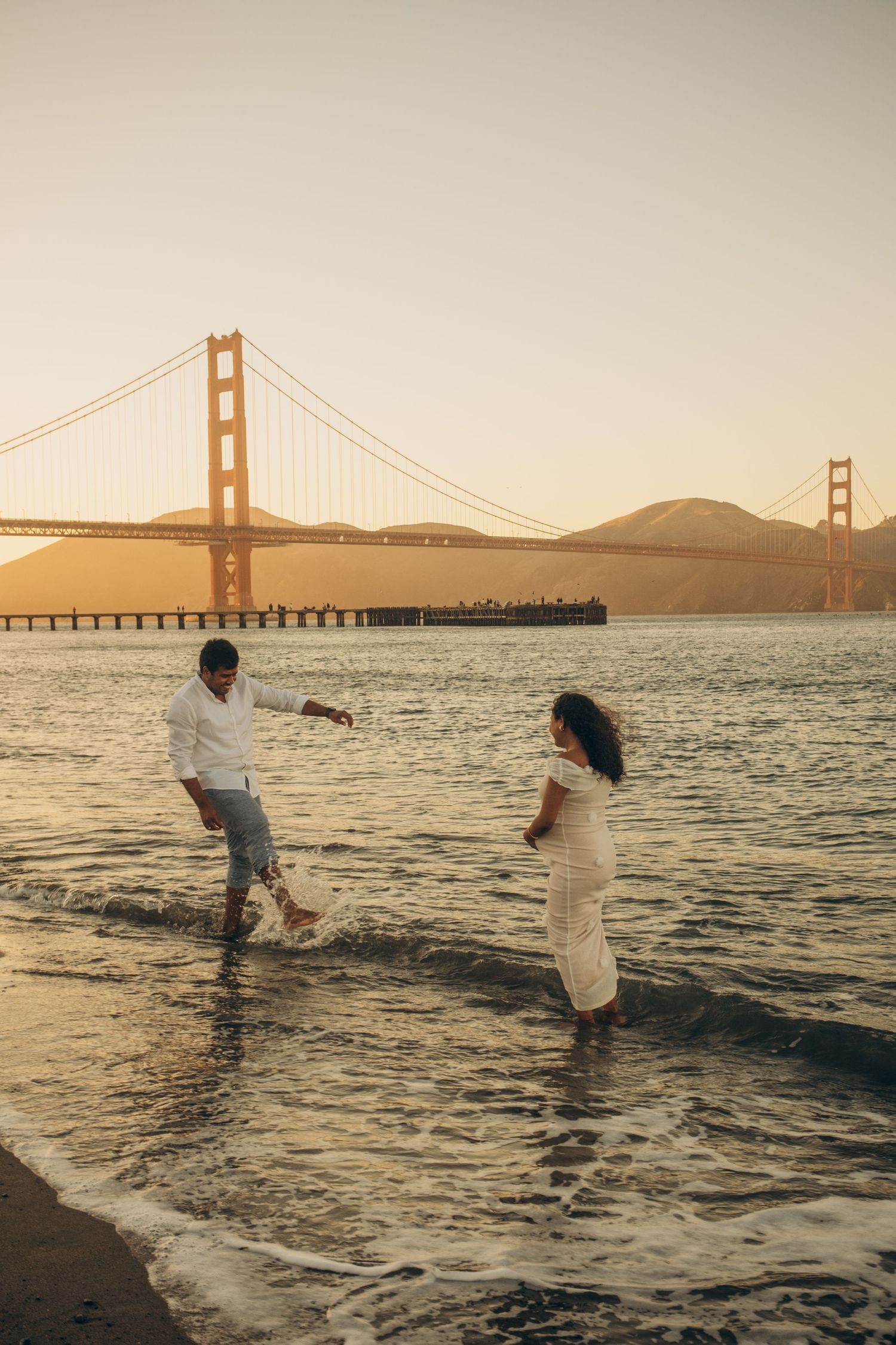 Couple splashing in the San Francisco Bay with Golden Gate Bridge in background.