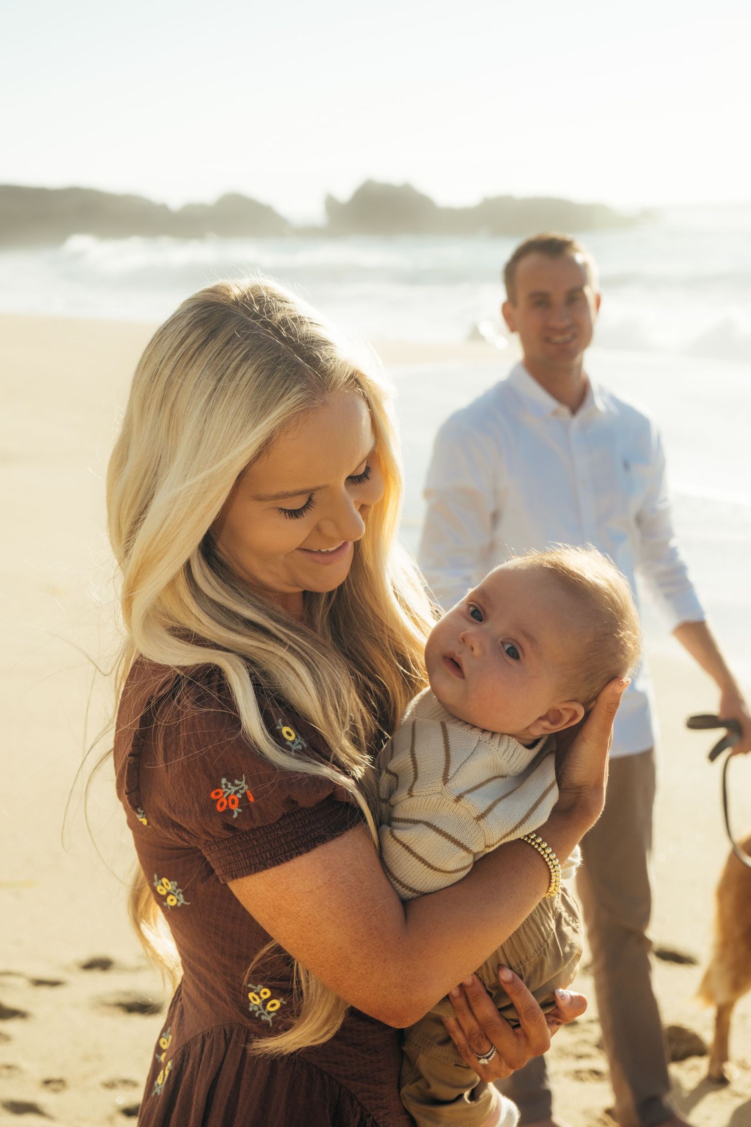 A warm family moment captured on a sunny beach with waves in the background.