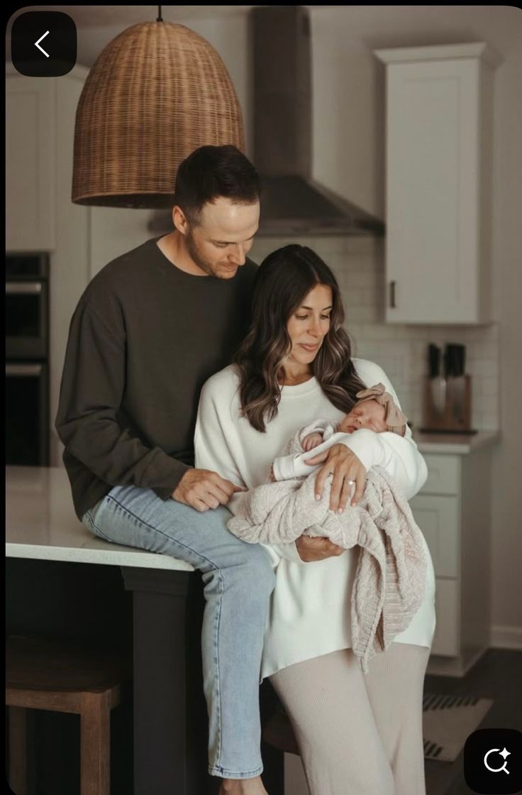 A couple shares tender moments with their newborn baby in a cozy home setting under a woven pendant light.