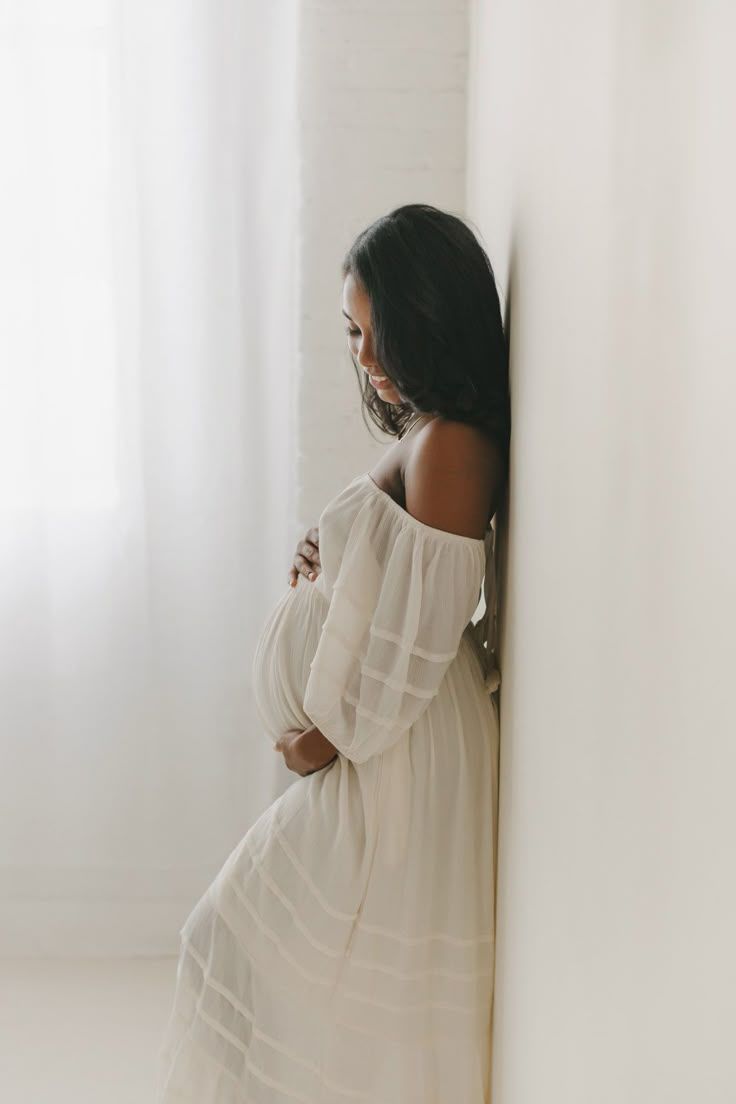 Artistic maternity portrait against white wall with flowing fabric and soft lighting.
