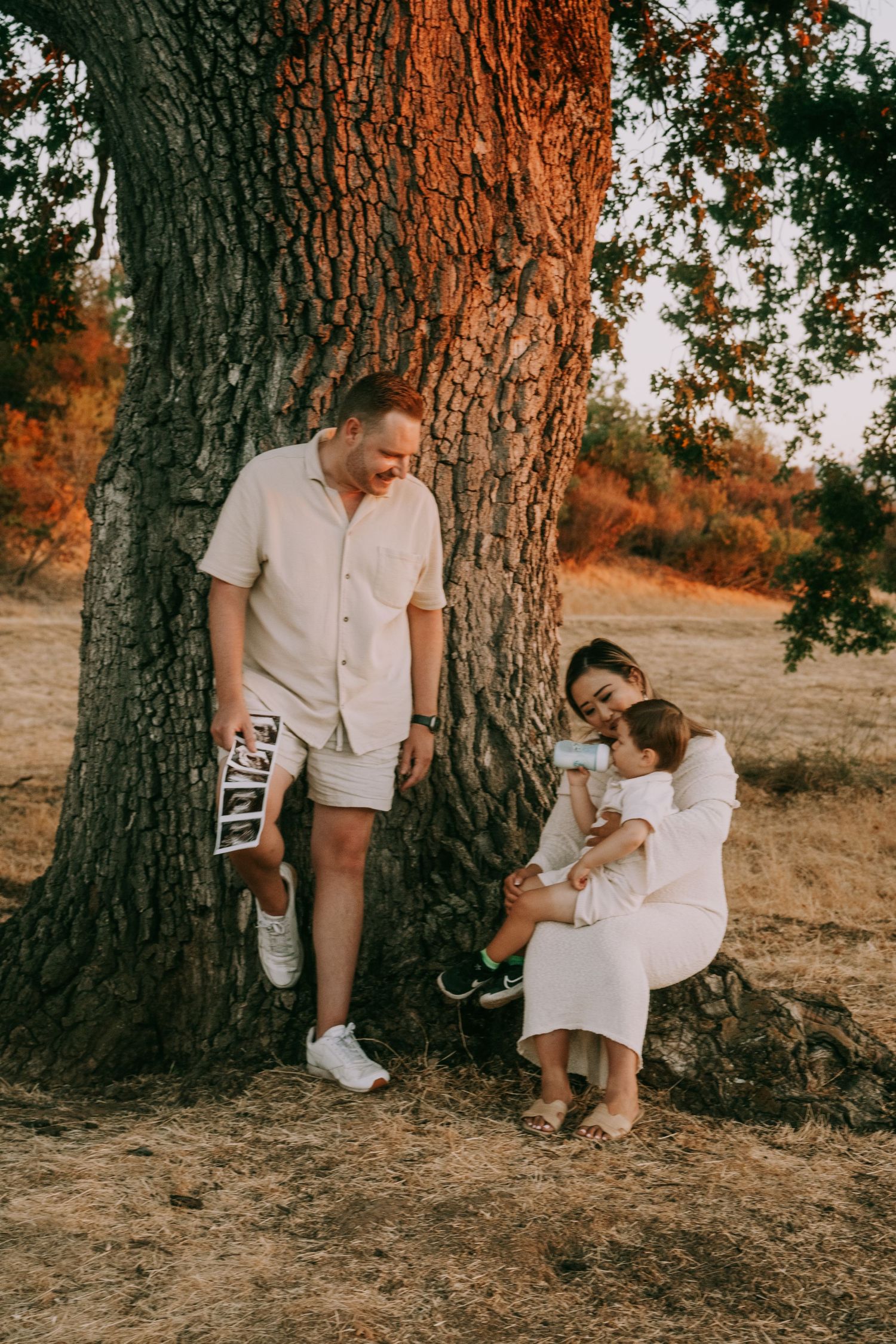 A family shares quiet moments together beneath a large tree trunk.