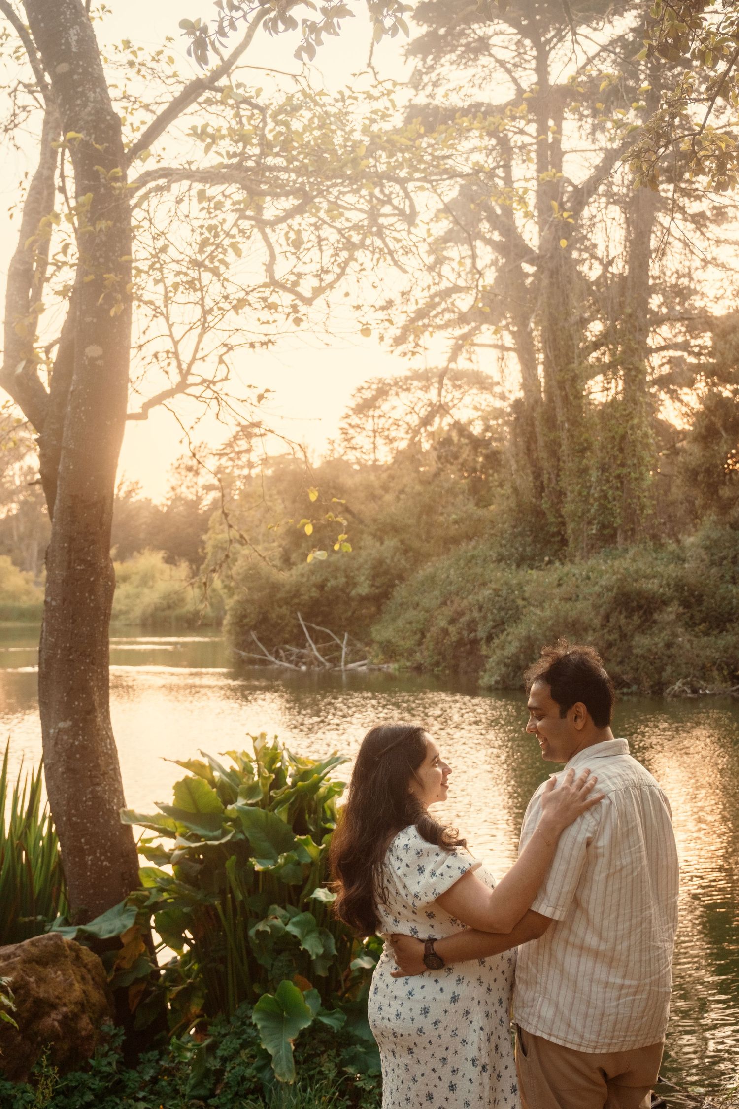 Couple sharing tender moments by a lake during golden hour.