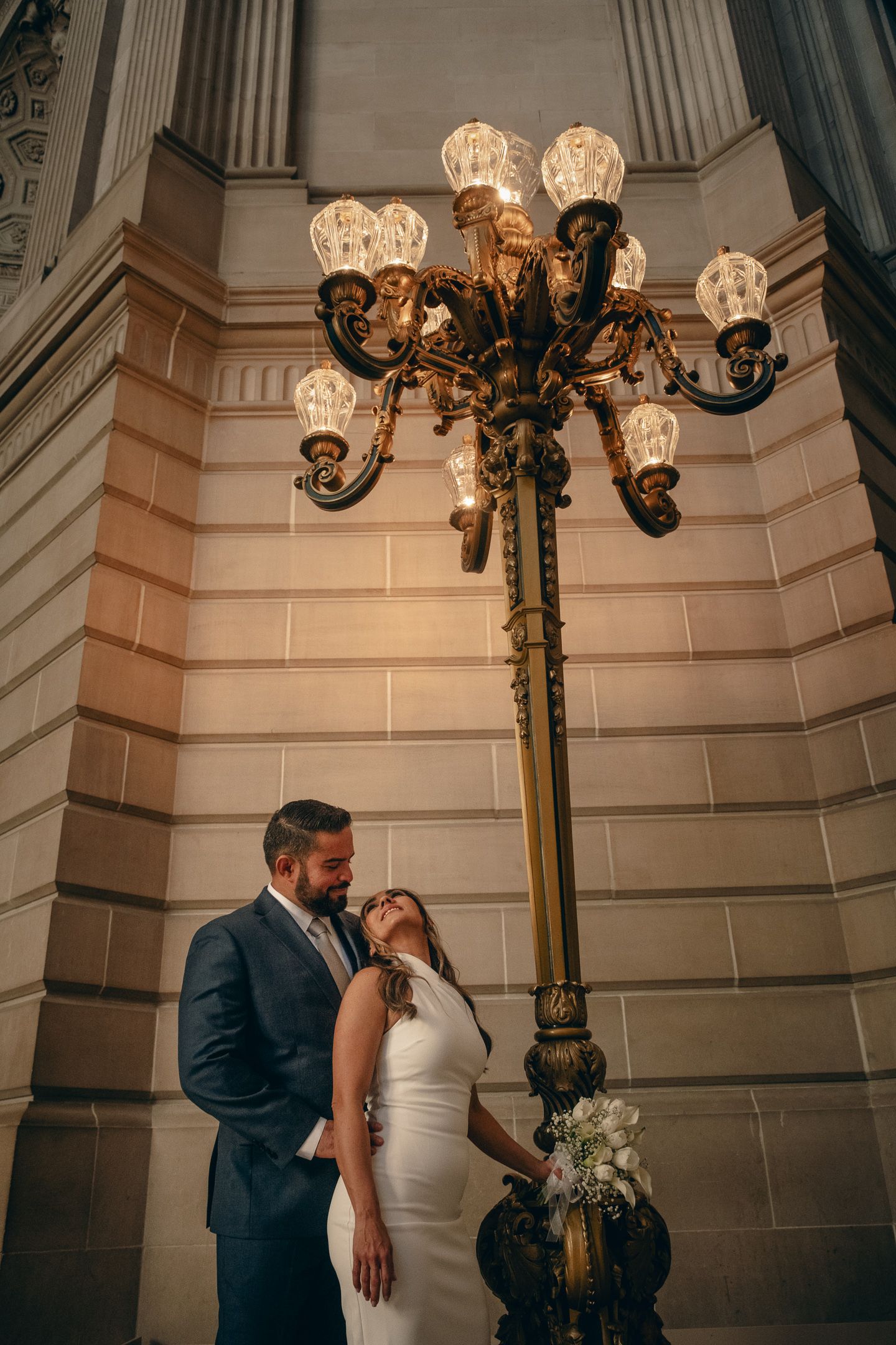 Intimate wedding portraits under ornate vintage light fixtures in a historic building.