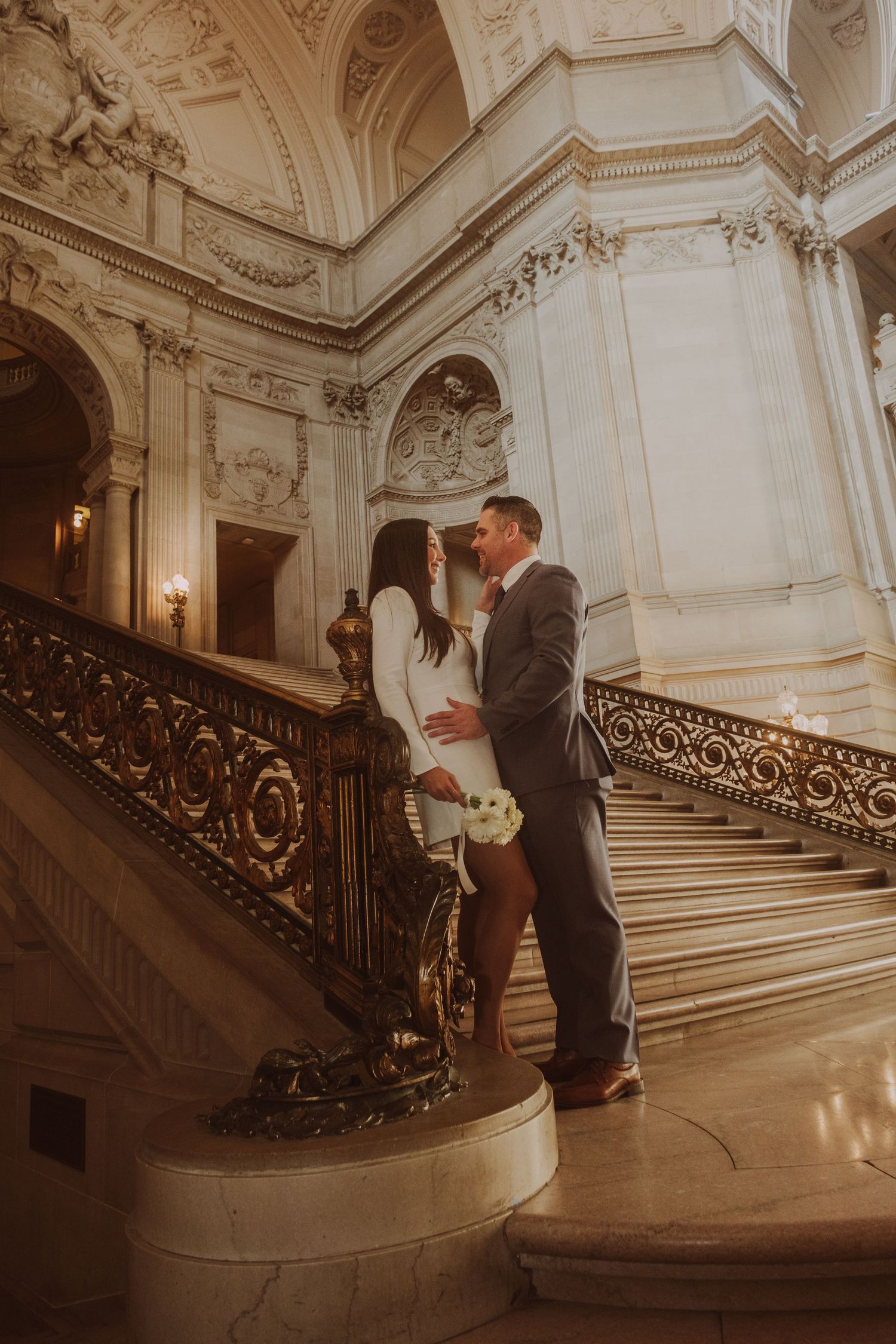 A romantic wedding moment on an ornate marble staircase in a grand historic building.