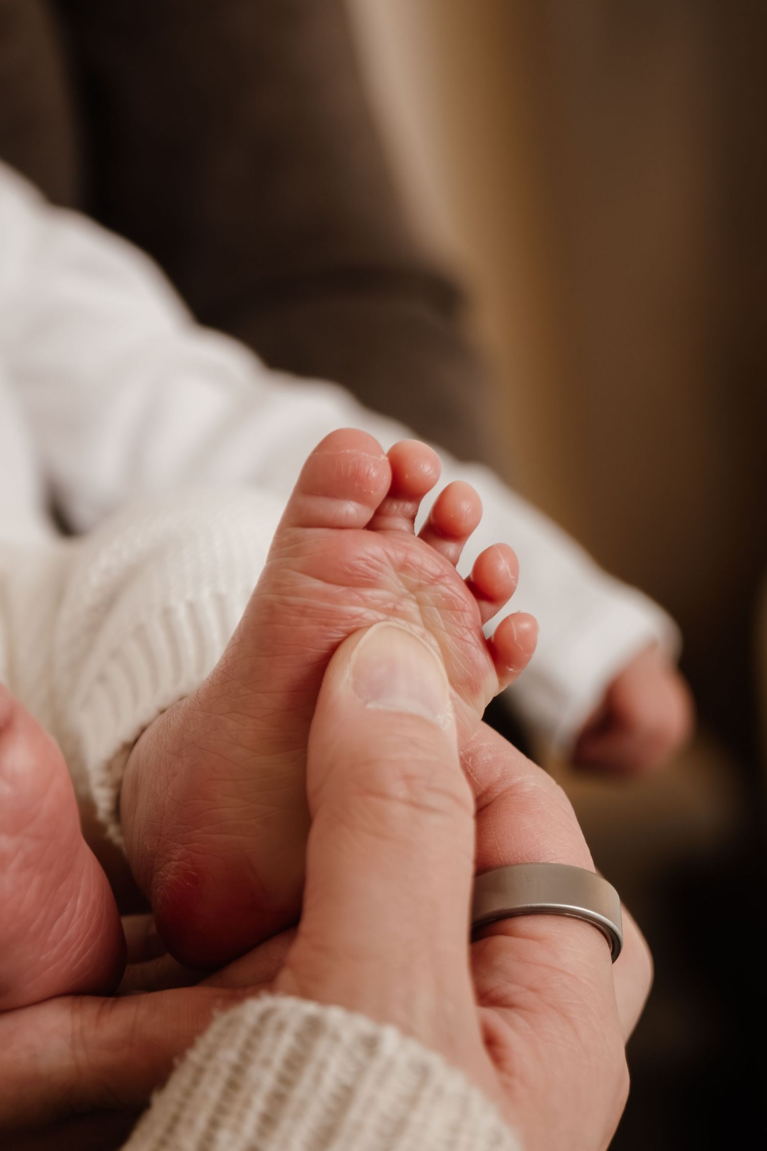 Close-up of a tiny baby's foot being gently held by an adult hand wearing a wedding ring.