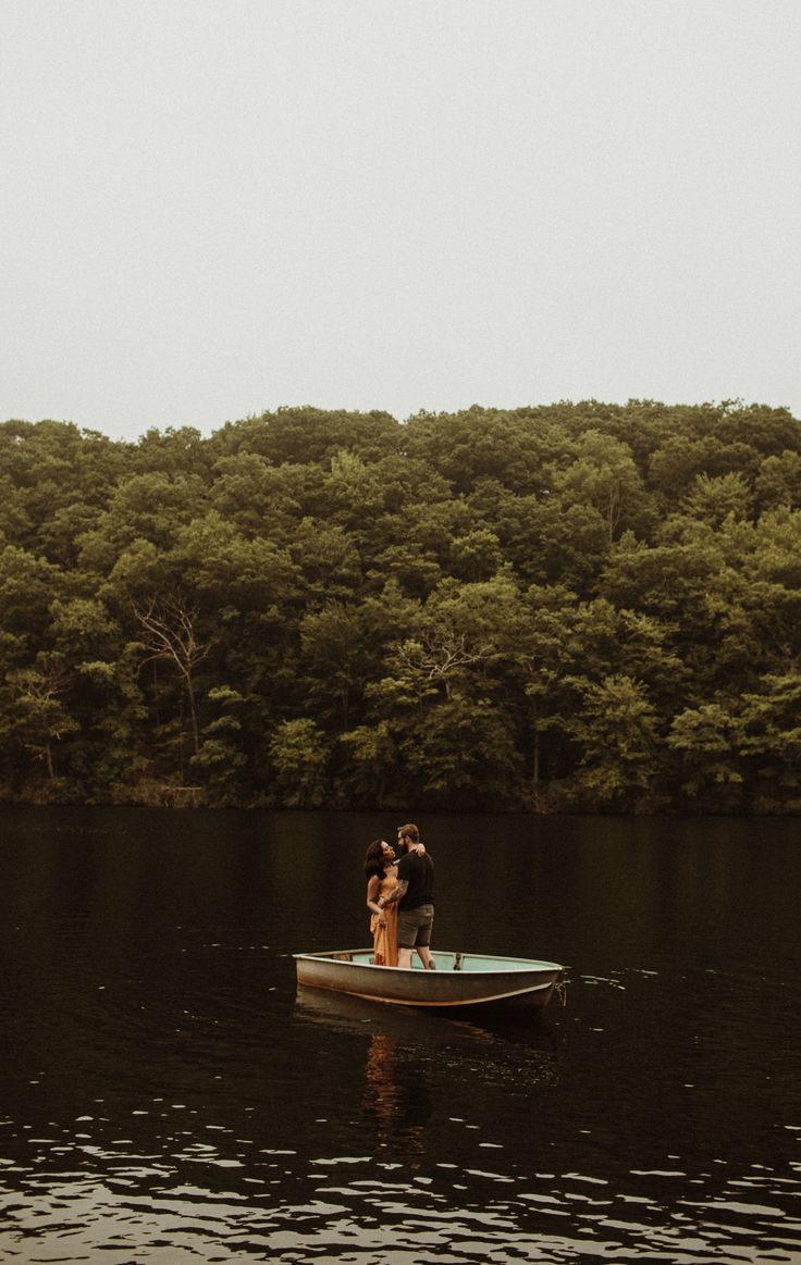 Small rowboat gliding across dark waters with tree-lined shore in background.