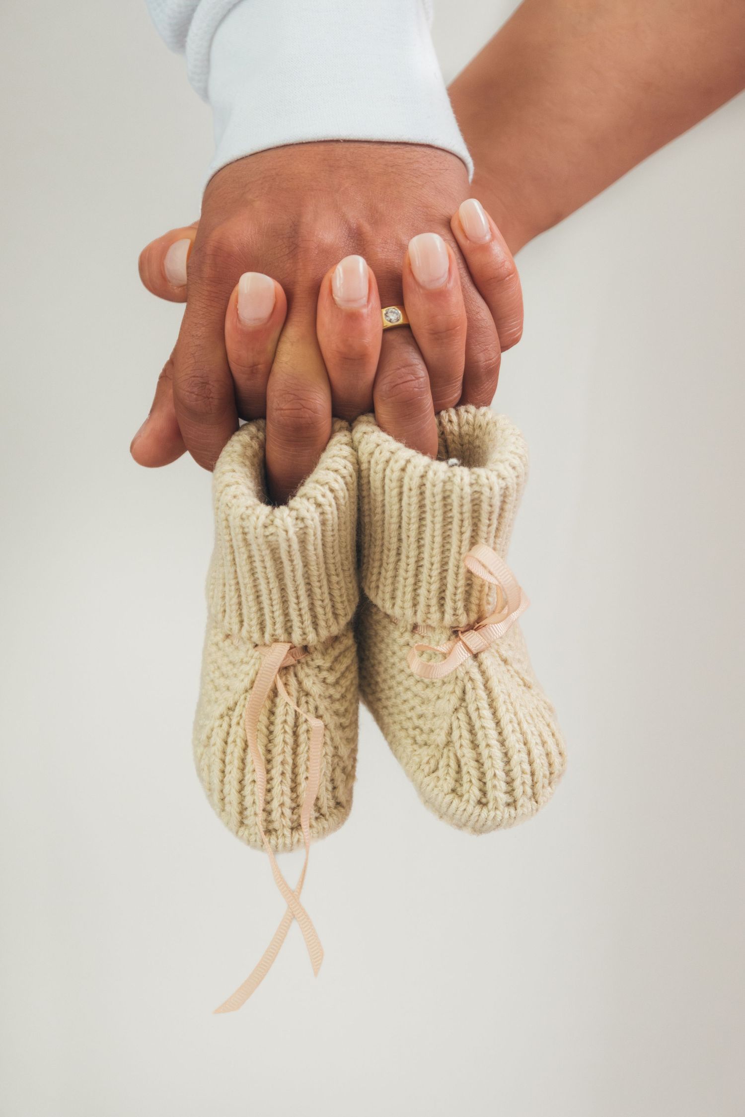 Hands holding small knitted beige baby booties against white background.