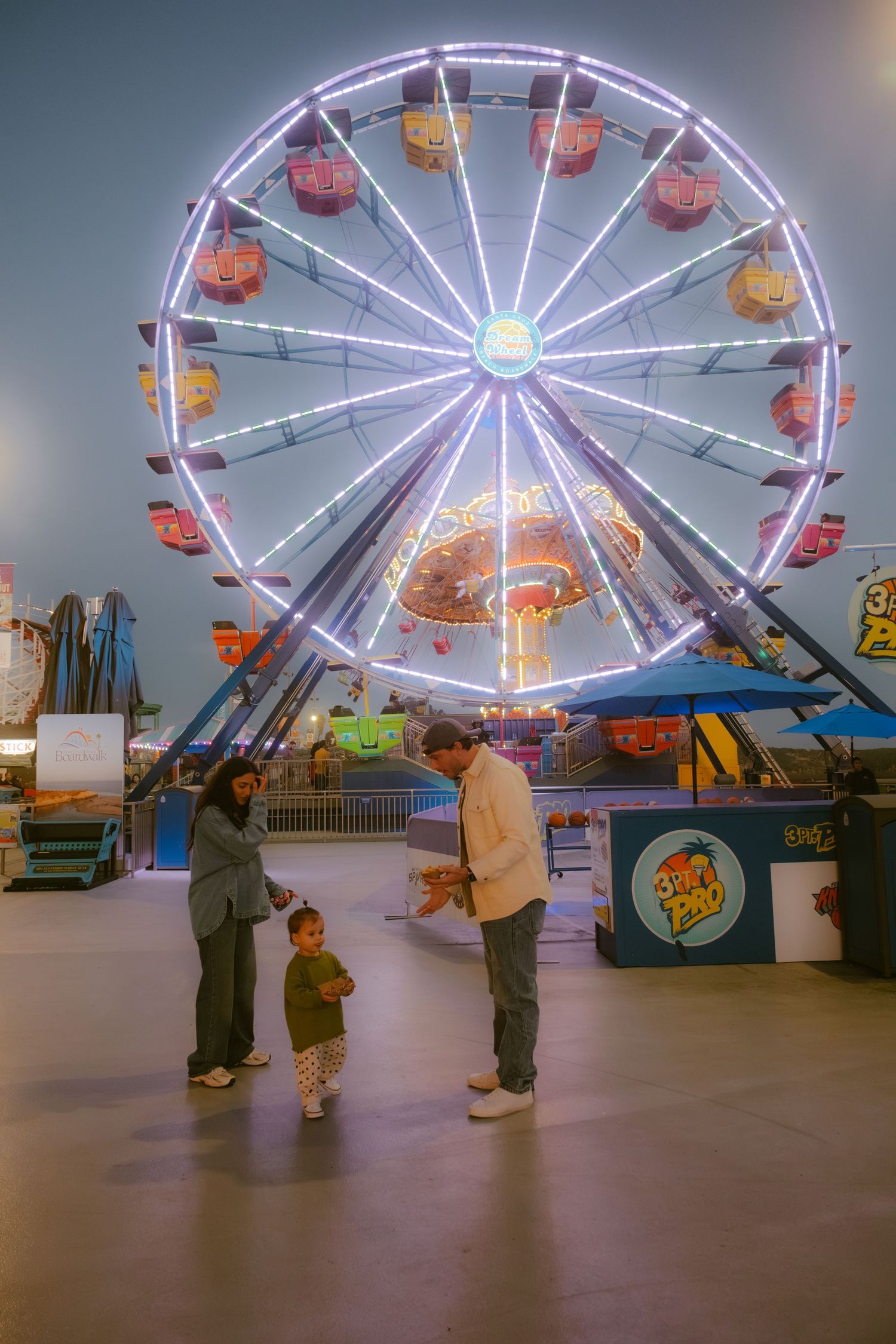 Family enjoying an indoor amusement park with a glowing Ferris wheel at night.