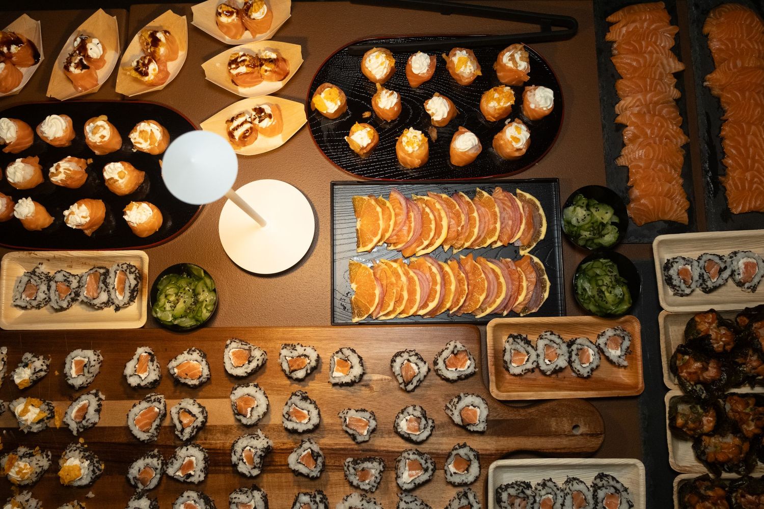 Overhead view of an elaborate sushi and appetizer spread on wooden boards with rolls, nigiri, and bite-sized canapés.