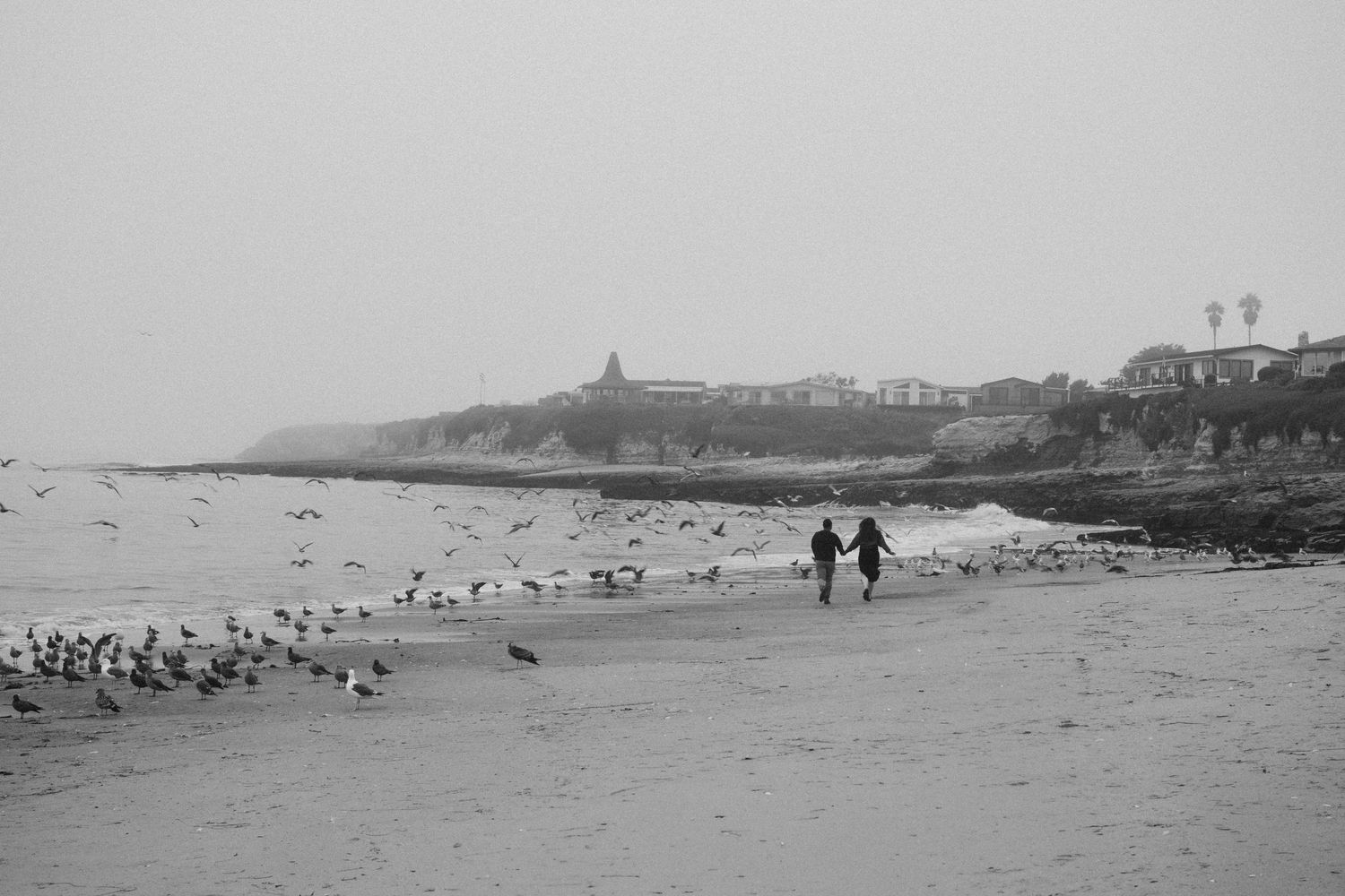 A panoramic view of a beach coastline with distant buildings and people.
