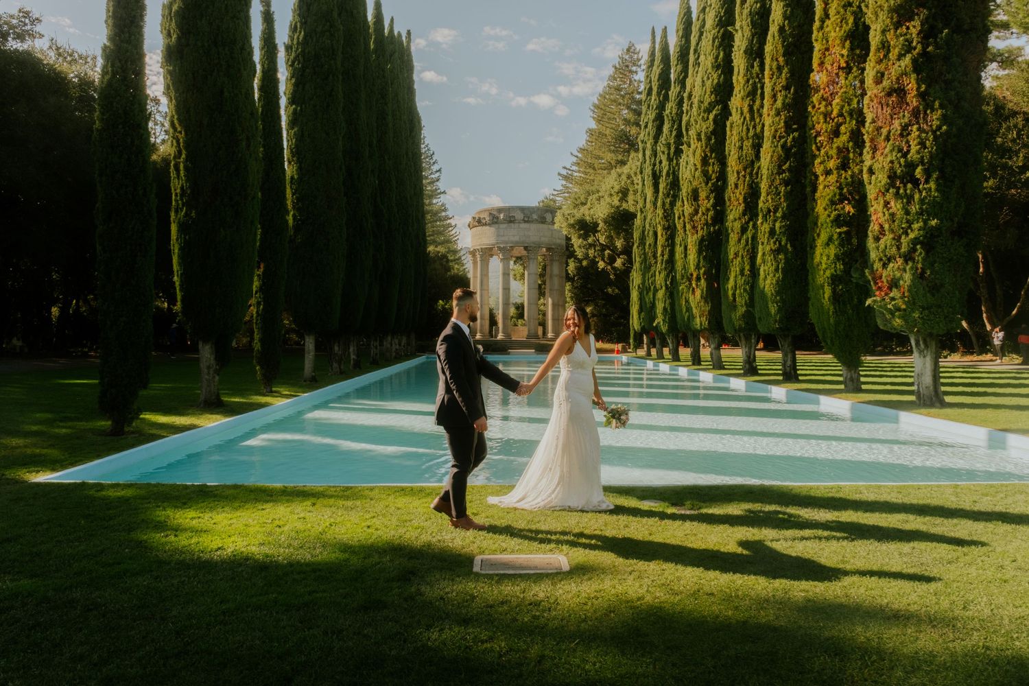 A scenic pathway lined with tall cypress trees and manicured lawns on a sunny afternoon.
