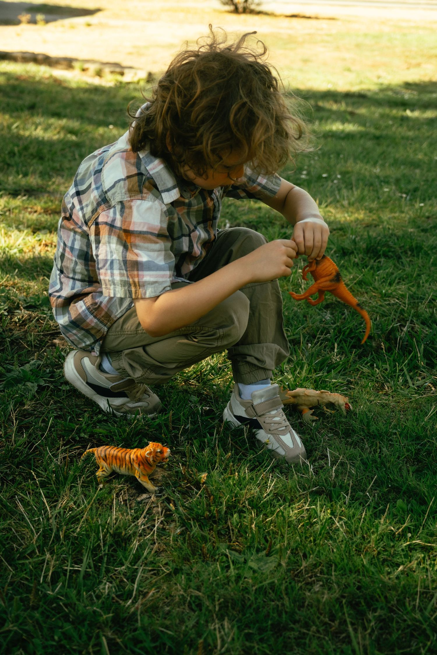 A child in a plaid shirt plays with toys on grass in golden sunlight.