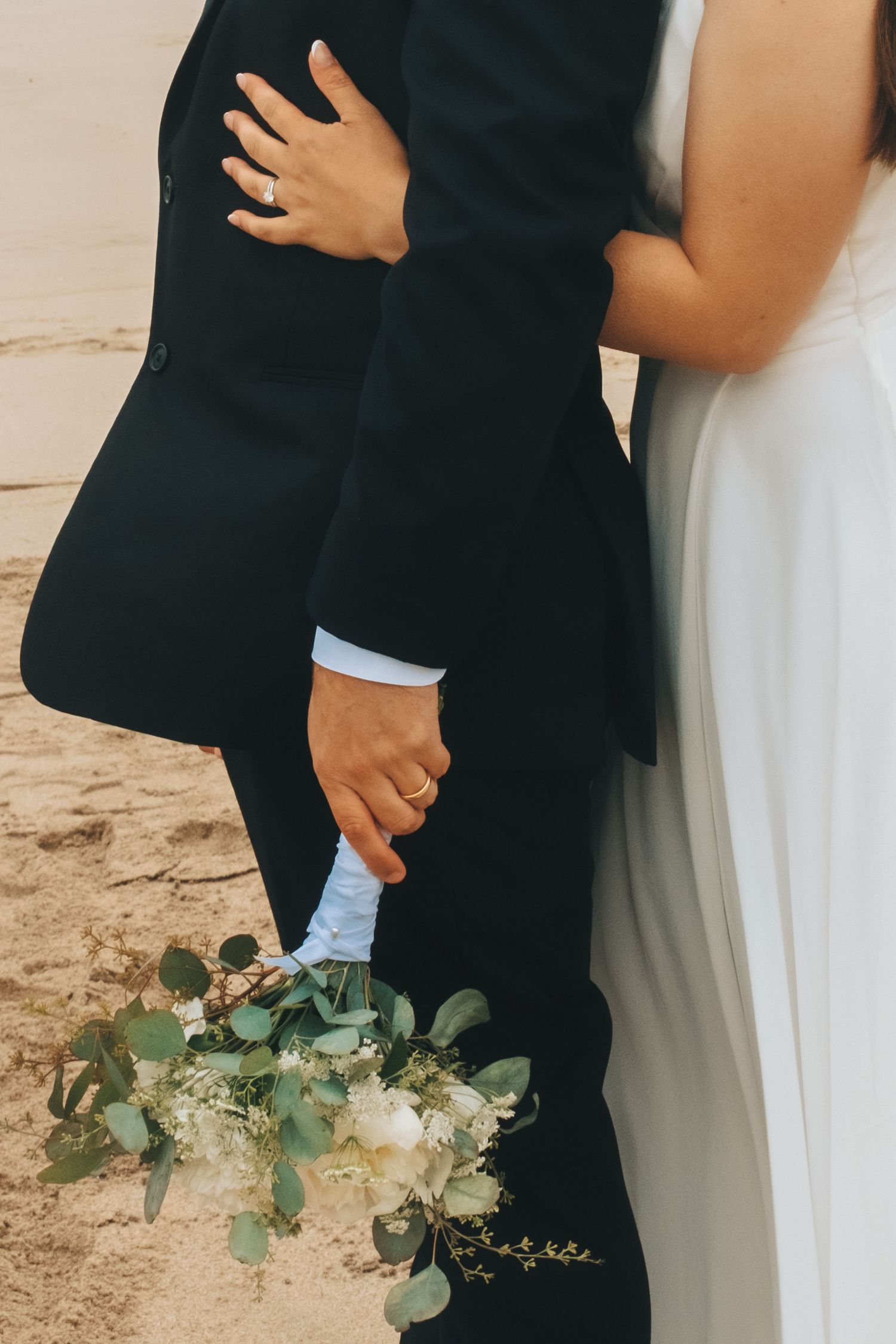 Close-up details of a wedding couple embracing, with a white floral bouquet visible.