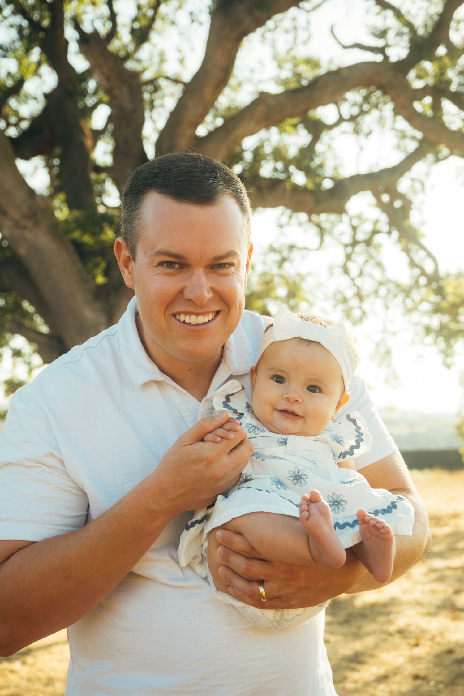 Joyful outdoor family photos with a smiling baby in white clothing.