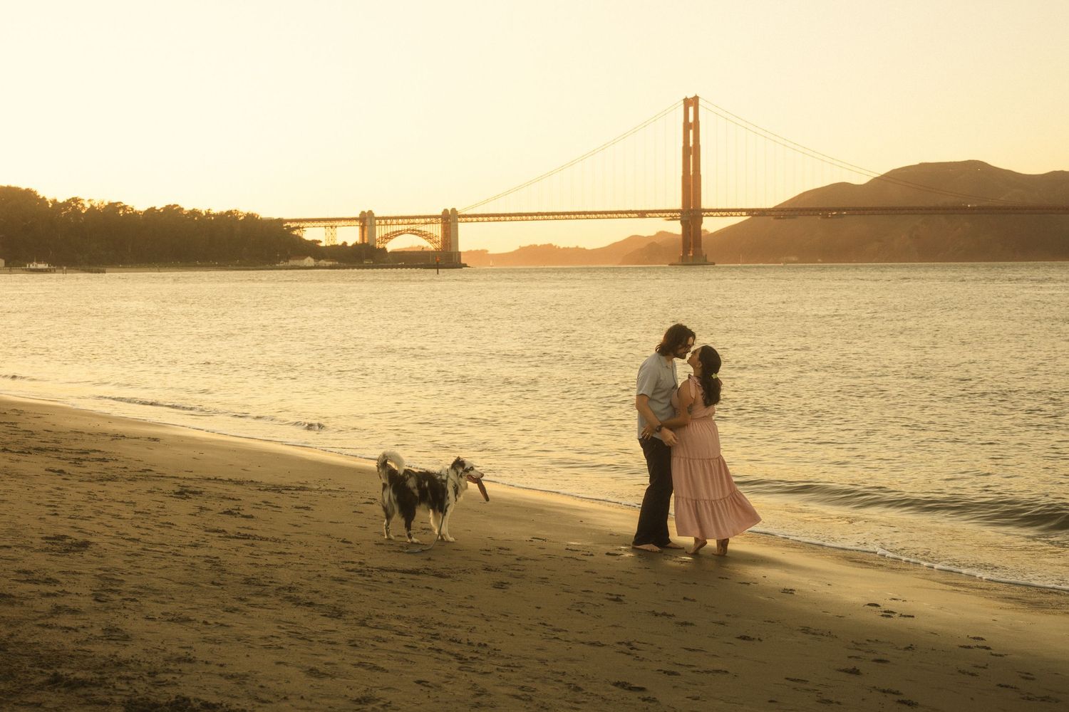 Romantic beach photoshoot with the Golden Gate Bridge visible in the distance at sunset.