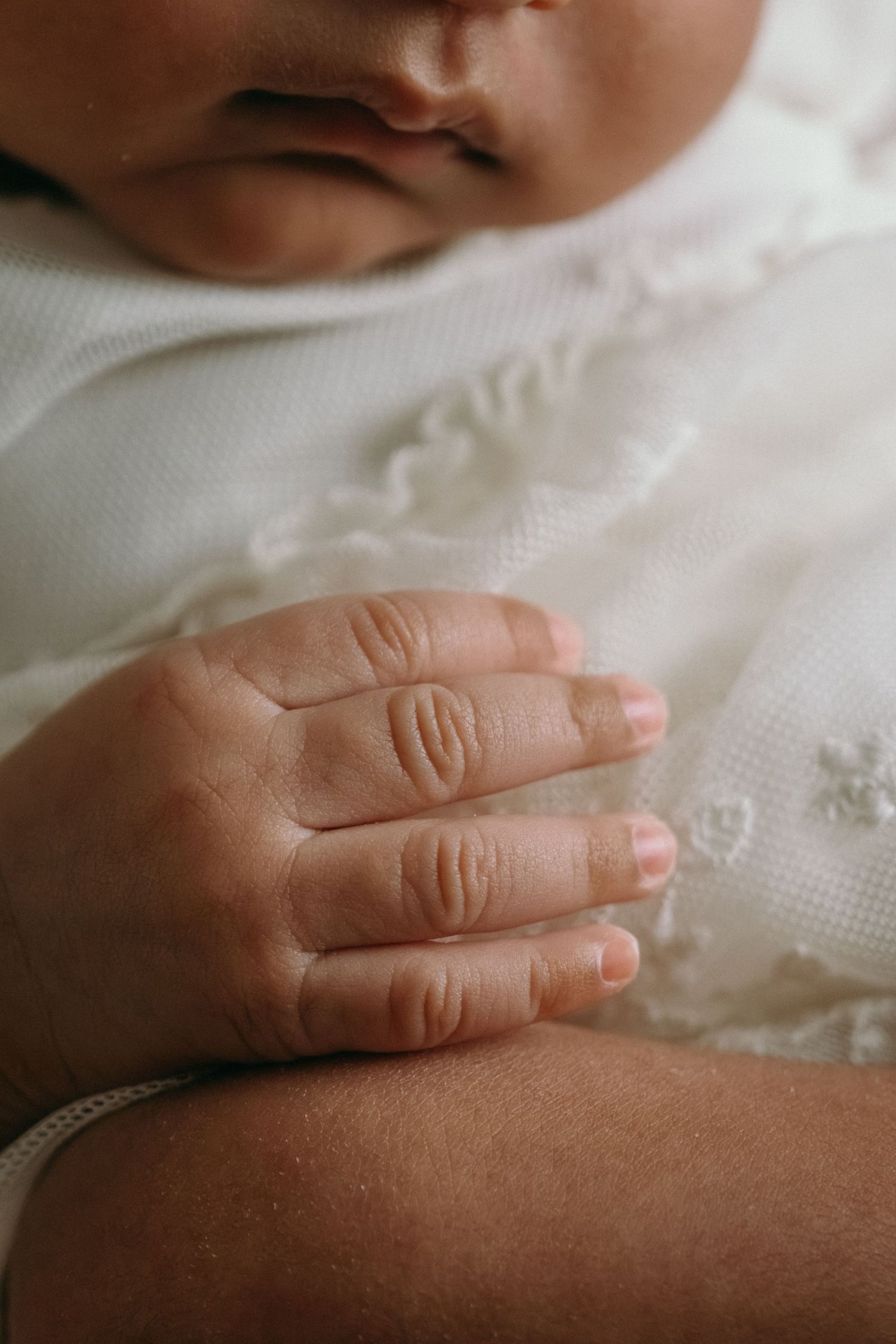 Tiny baby hand resting on white textured fabric in natural light.