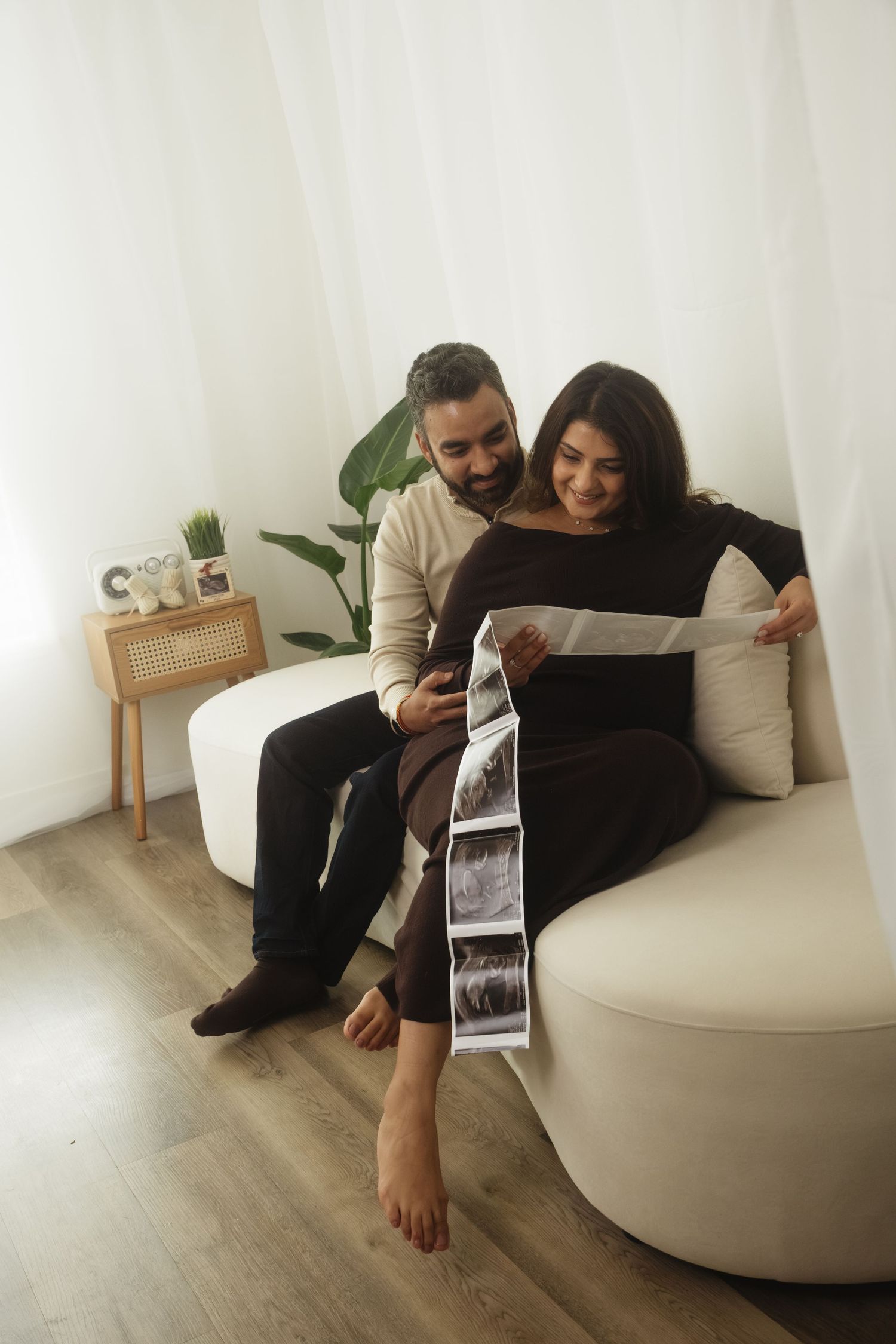 A couple looks at ultrasound photos while relaxing on a white couch.