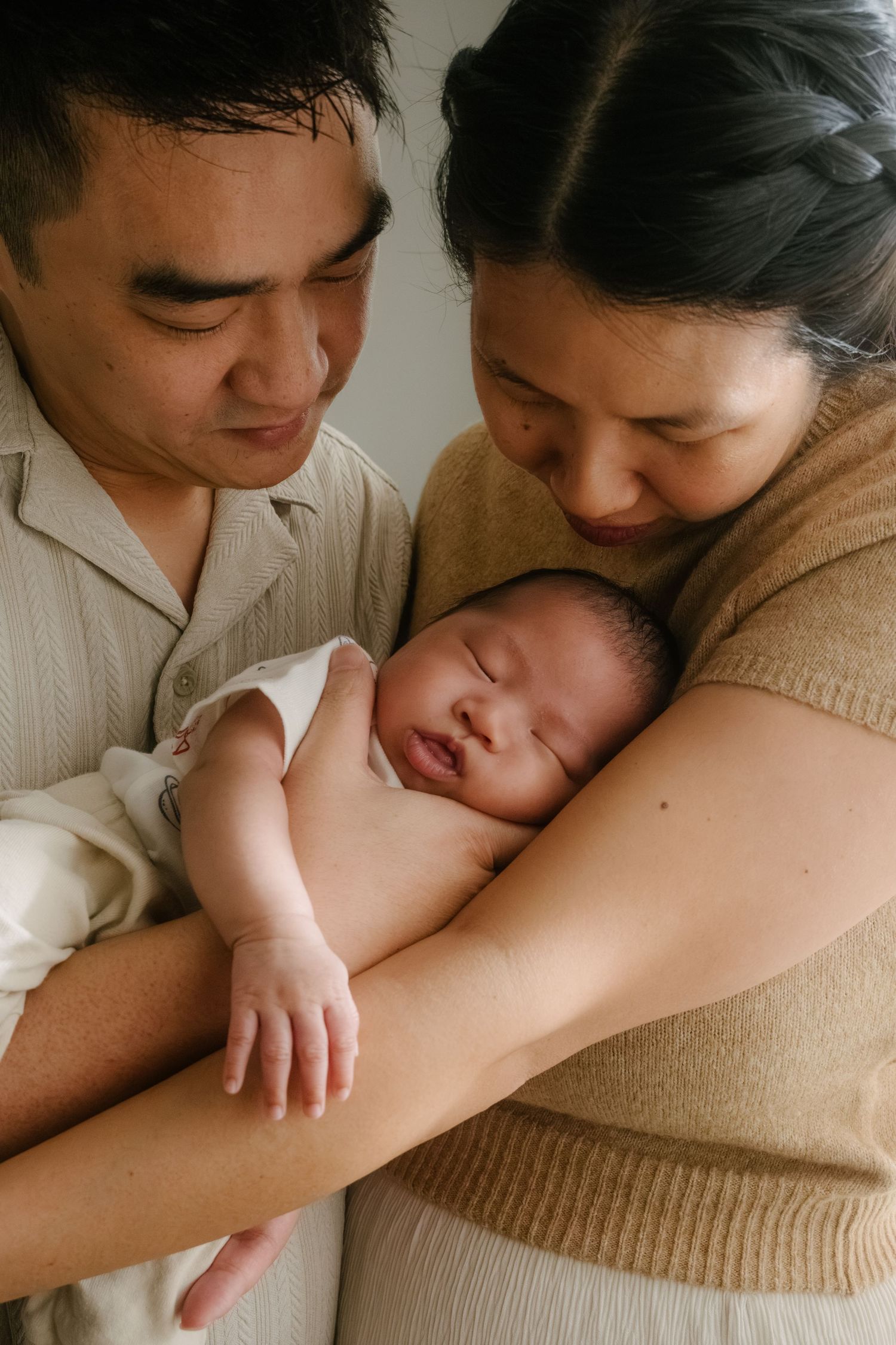 Two parents lovingly cradle their sleeping newborn baby, sharing a tender family moment together.