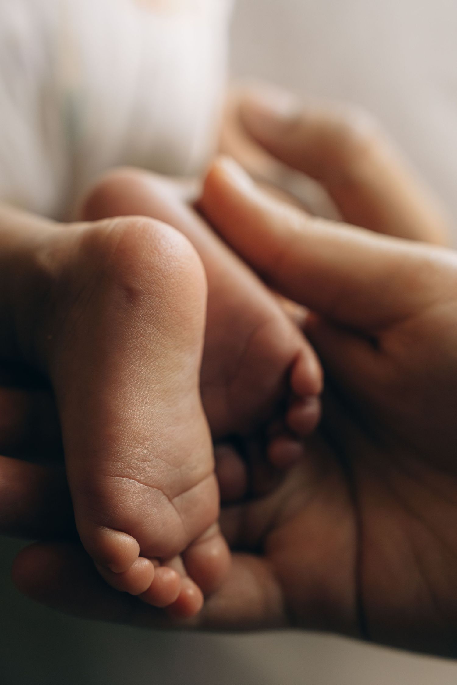 Adult hands gently cradling tiny newborn baby feet in a tender close-up moment.